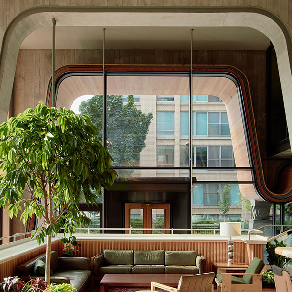 Modern lounge area with curved window, green plants, and olive sofa beneath architectural archway