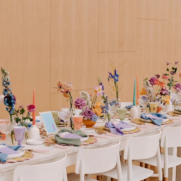 A bright, colorful event table setting with pastel floral arrangements and white modern chairs.