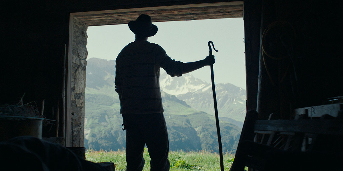 A silhouette of a shepherd standing at the doorway looking out towards the green grassy hills and mountains