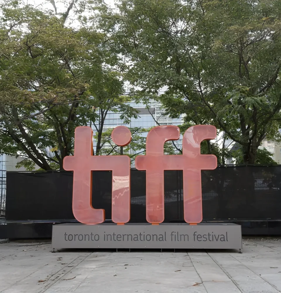 Large orange TIFF logo sign for the Toronto International Film Festival outdoors with trees behind it.