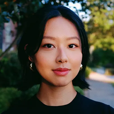 Asian woman with short black hair and red lipstick smiling outdoors in natural lighting