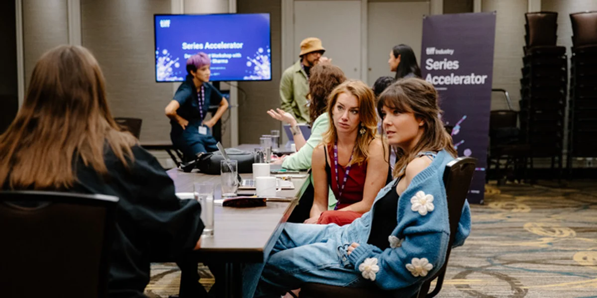People seated at a conference table during Series Accelerator event with presentation screen in background