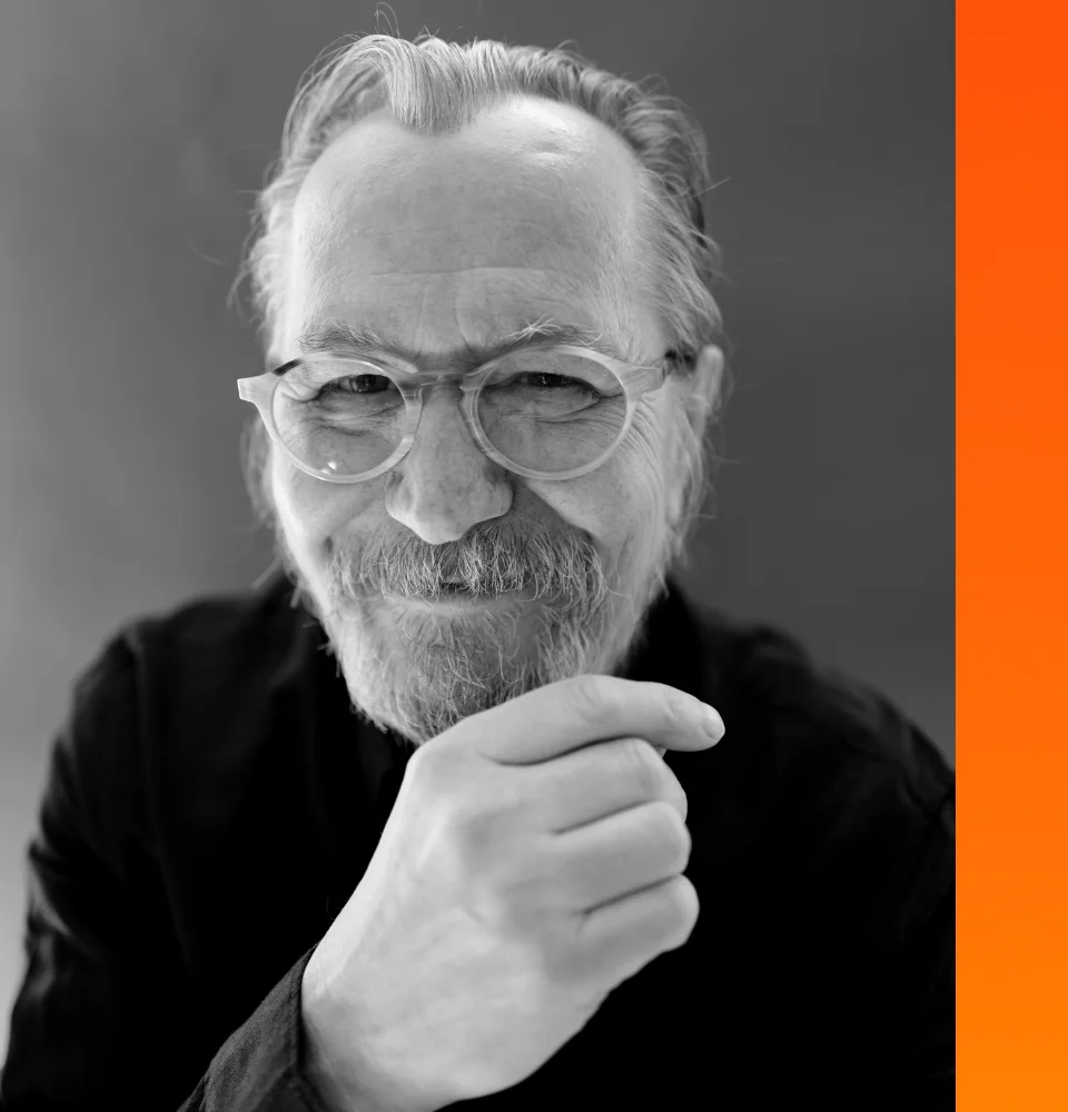 Black and white portrait of an older man with glasses and a beard, smiling with hand near chin.