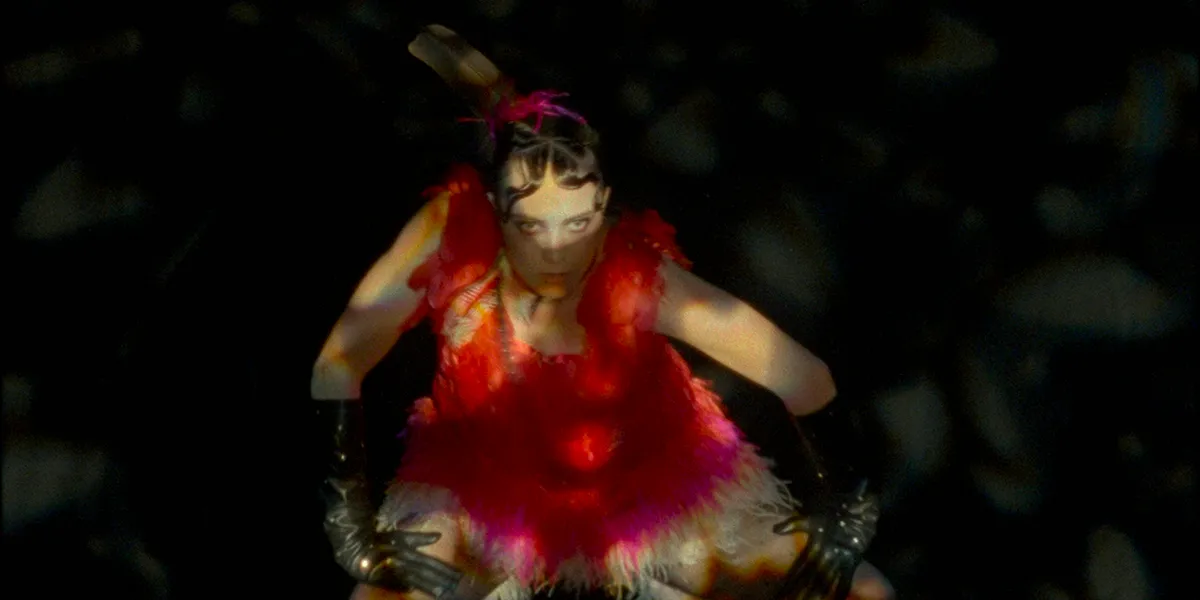 Dancer in vibrant red costume performing against dark background, dramatic lighting creates ethereal effect