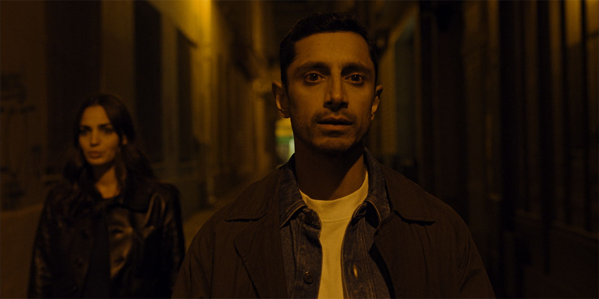 Riz Ahmed standing in a dark alley looking off camera from the short, DAMMI