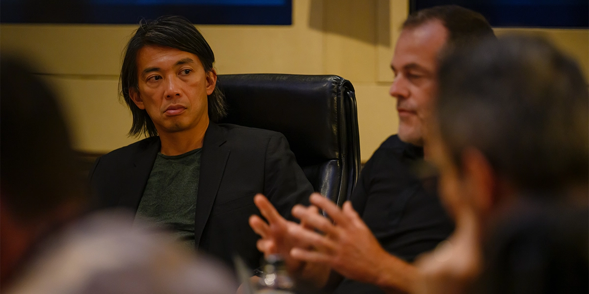 Mid-shot photo of participants at a roundtable event, with one attendee listening closely to another speaker in the foreground.