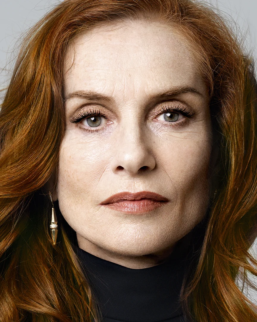 Close-up portrait of a woman with red hair, green eyes, gold earrings, and a black turtleneck.