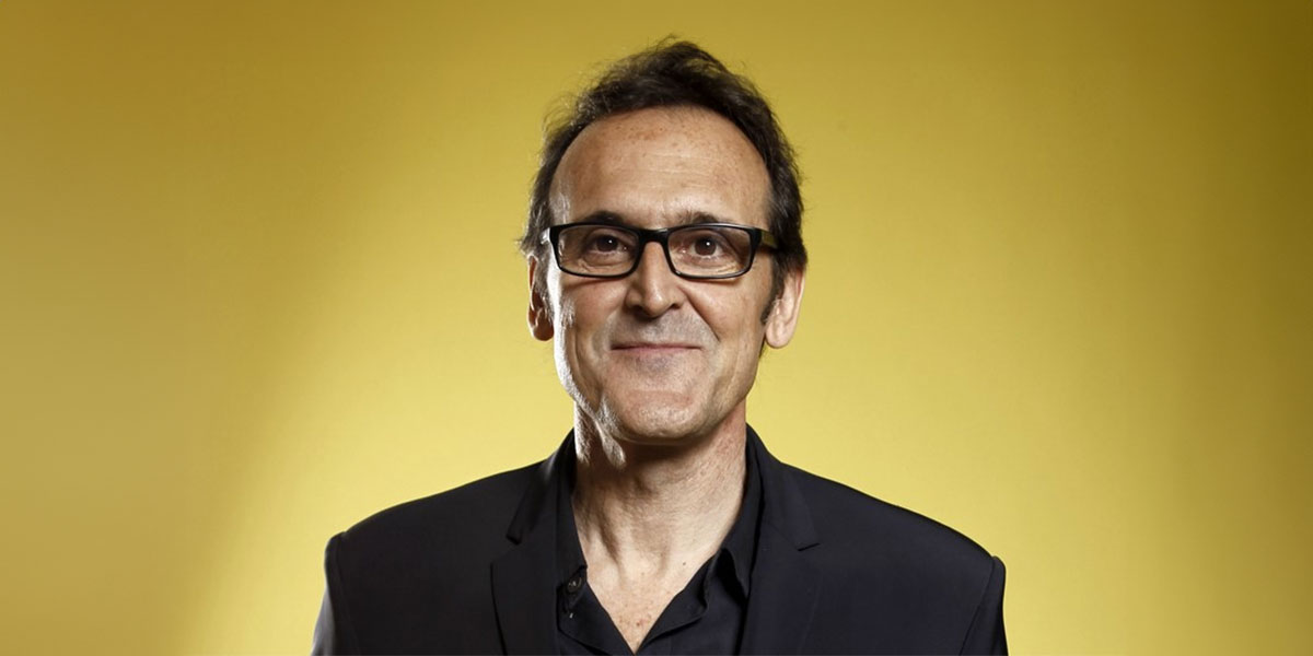 Portait of Alberto Iglesias in a black suit against a golden background