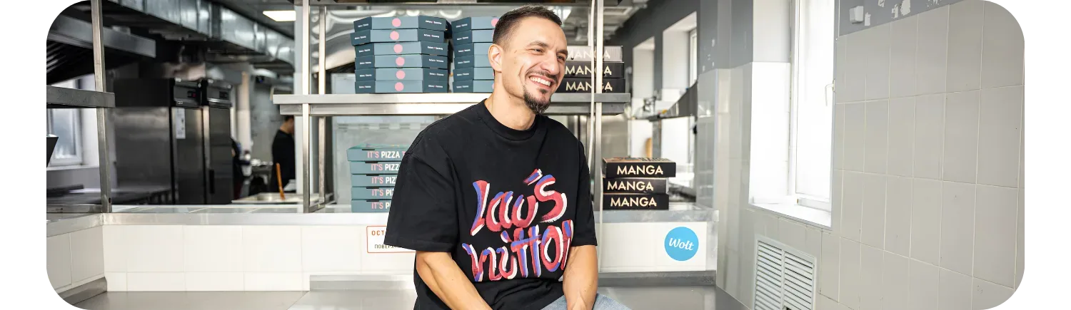 Manga Sushi founder Maxim Bortnikov smiling in the kitchen surrounded by Wolt delivery boxes.