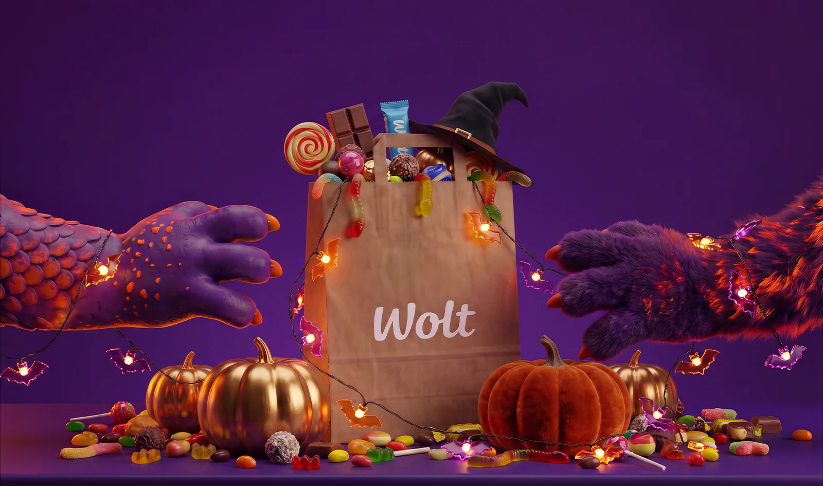 Wolt paper delivery bag overflowing with lollipops, chocolate, gummy worms and a witch hat, surrounded by golden and orange pumpkins, scattered candy and glowing bat string lights, with two monster hands reaching for the bag on a purple background.