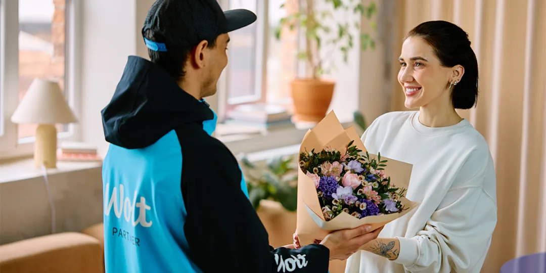 A Wolt delivery courier handing a flower bouquet to a customer at home.