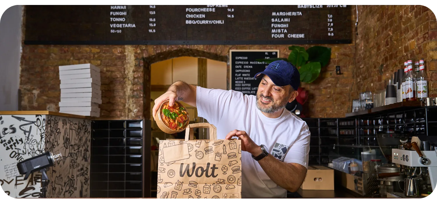 Ein Restaurantbesitzer legt ein frisch zubereitetes Gericht in eine Wolt-Liefertüte an der Theke, bereit zur Abholung durch einen Kurierpartner