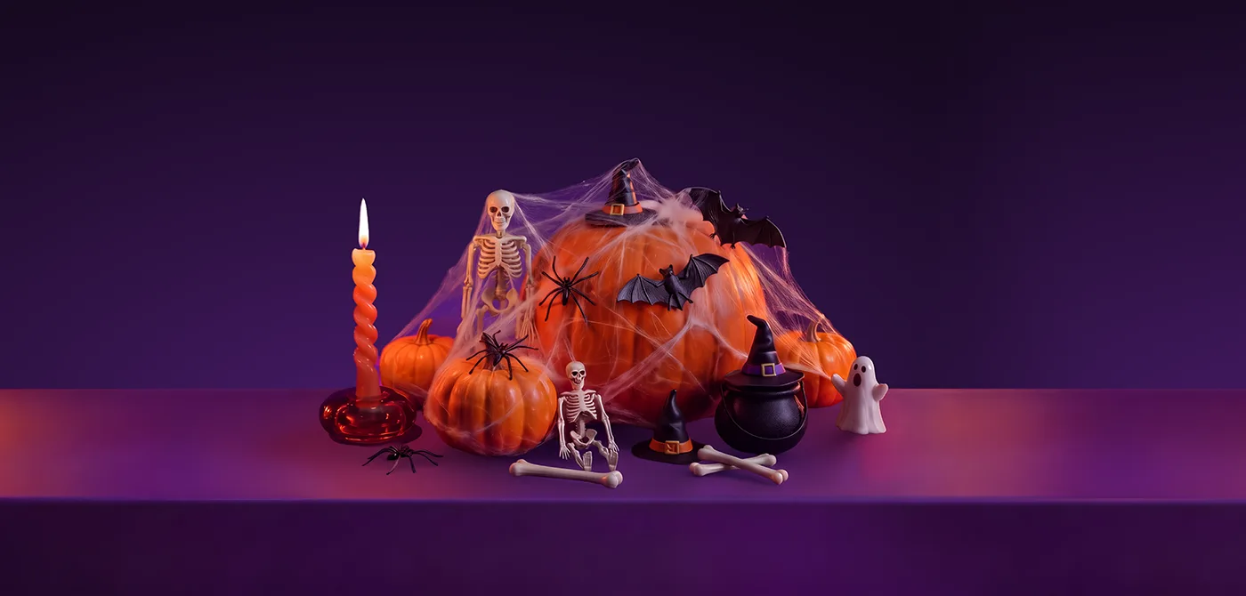 A pile of pumpkins wrapped in spiderweb with a toy bat and spiders, two small skeleton figurines, a black cauldron and two witch hats, beside a lit spiral candle, on a purple surface, representing Halloween party essentials delivered with Wolt.