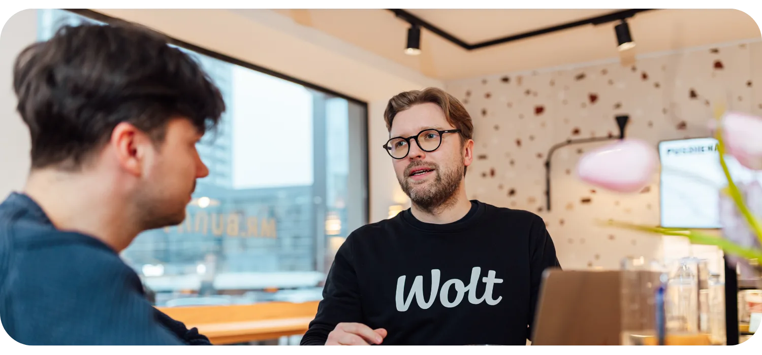 Ein Mann im schwarzen Wolt-Sweatshirt unterhält sich mit einer anderen Person am Tisch
