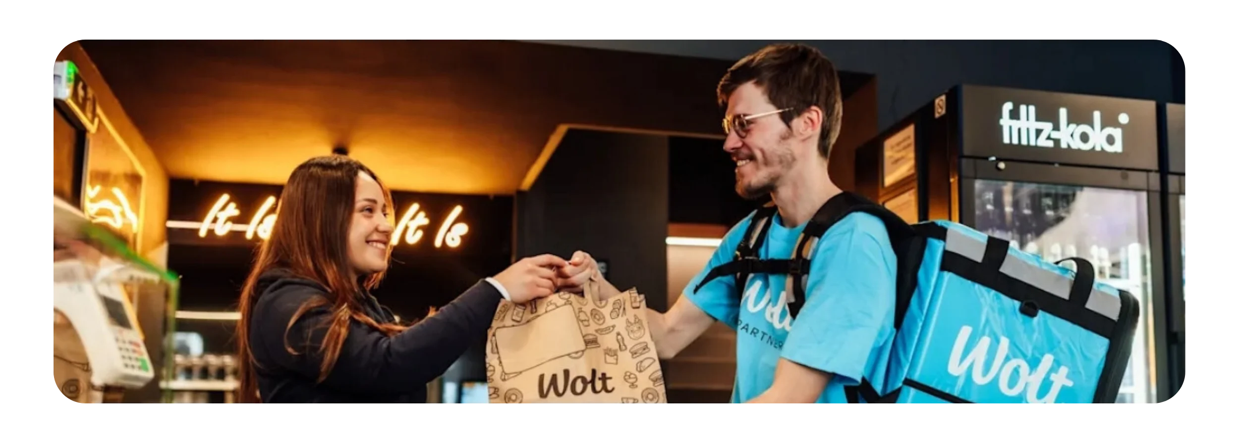 Eine Restaurantmitarbeiterin übergibt eine Wolt-Liefertüte an einen Wolt-Kurierpartner – für einen reibungslosen Bestellablauf bei der Essenslieferung