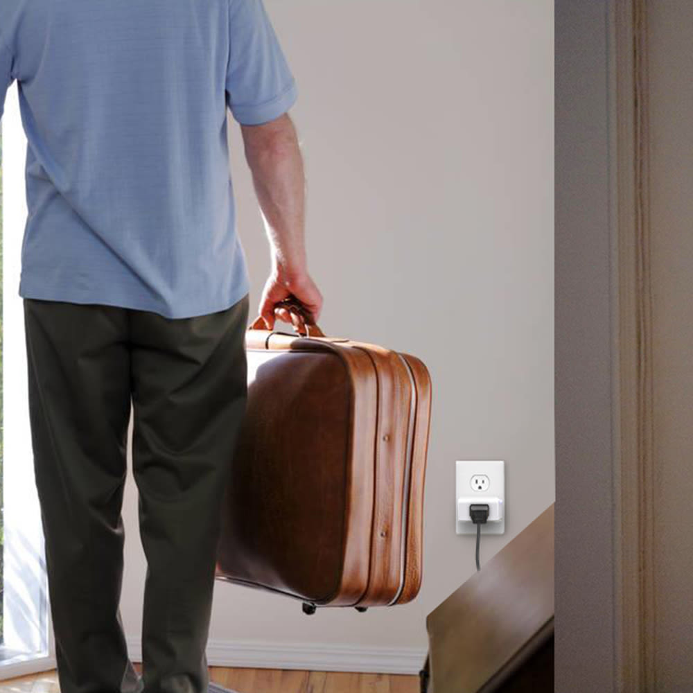 Personne portant une valise et se tenant à côté d’une prise intelligente Wi-Fi mini de Kasa branchée à une prise murale