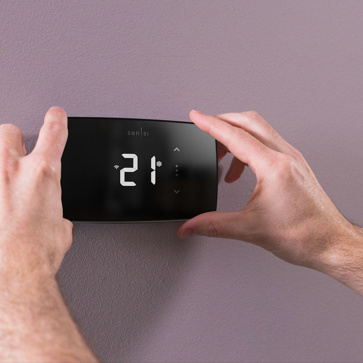 Une personne réglant la température sur un thermostat intelligent Sensi Lite.
