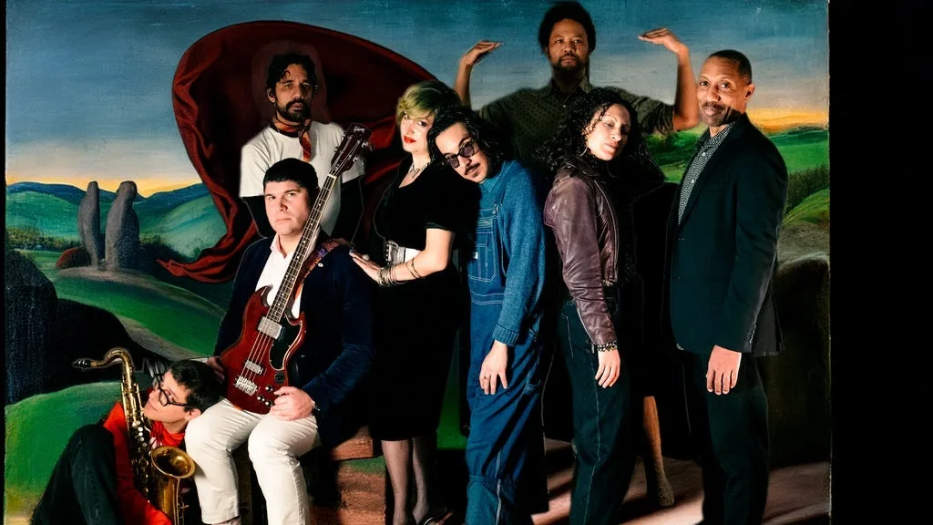 A diverse music group posing dramatically against a surreal green landscape backdrop with instruments and stylish attire.