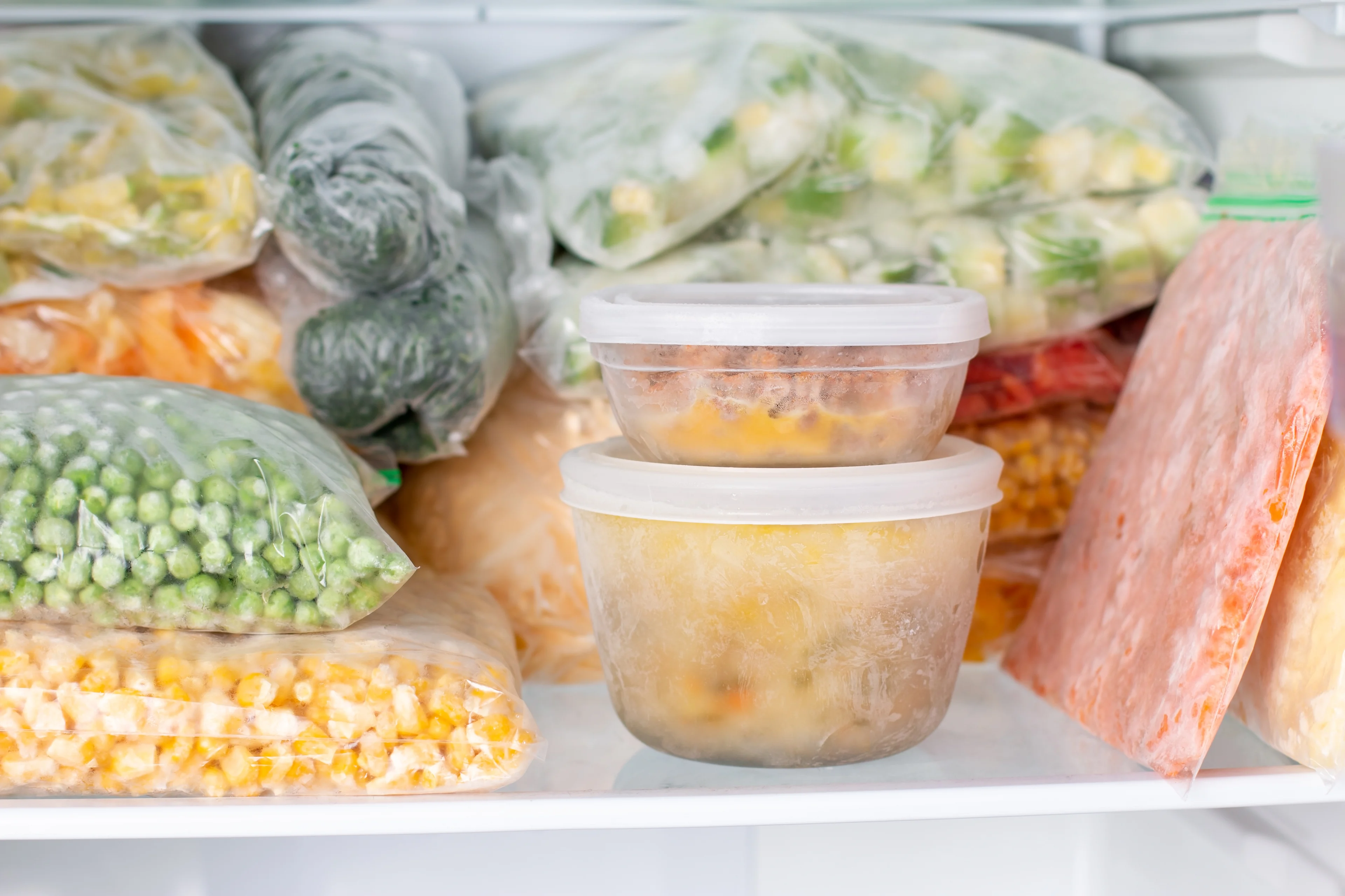 Frozen vegetables and prepared meals in plastic bags and containers stored in a freezer, showing meal prep organization.