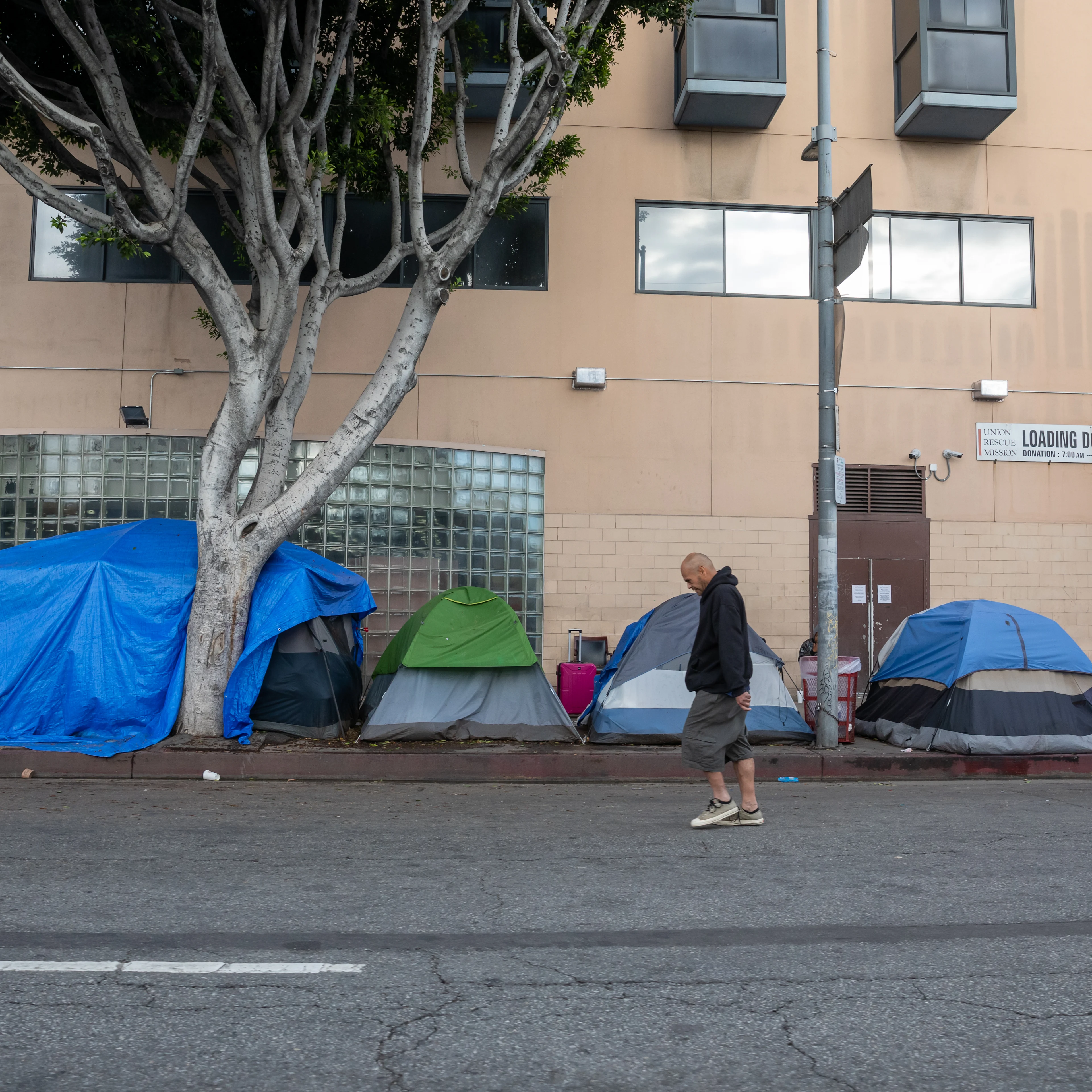 A man walks along a line of multi-colored tents on a sidewalk in the Skid Row district of downtown Los Angeles