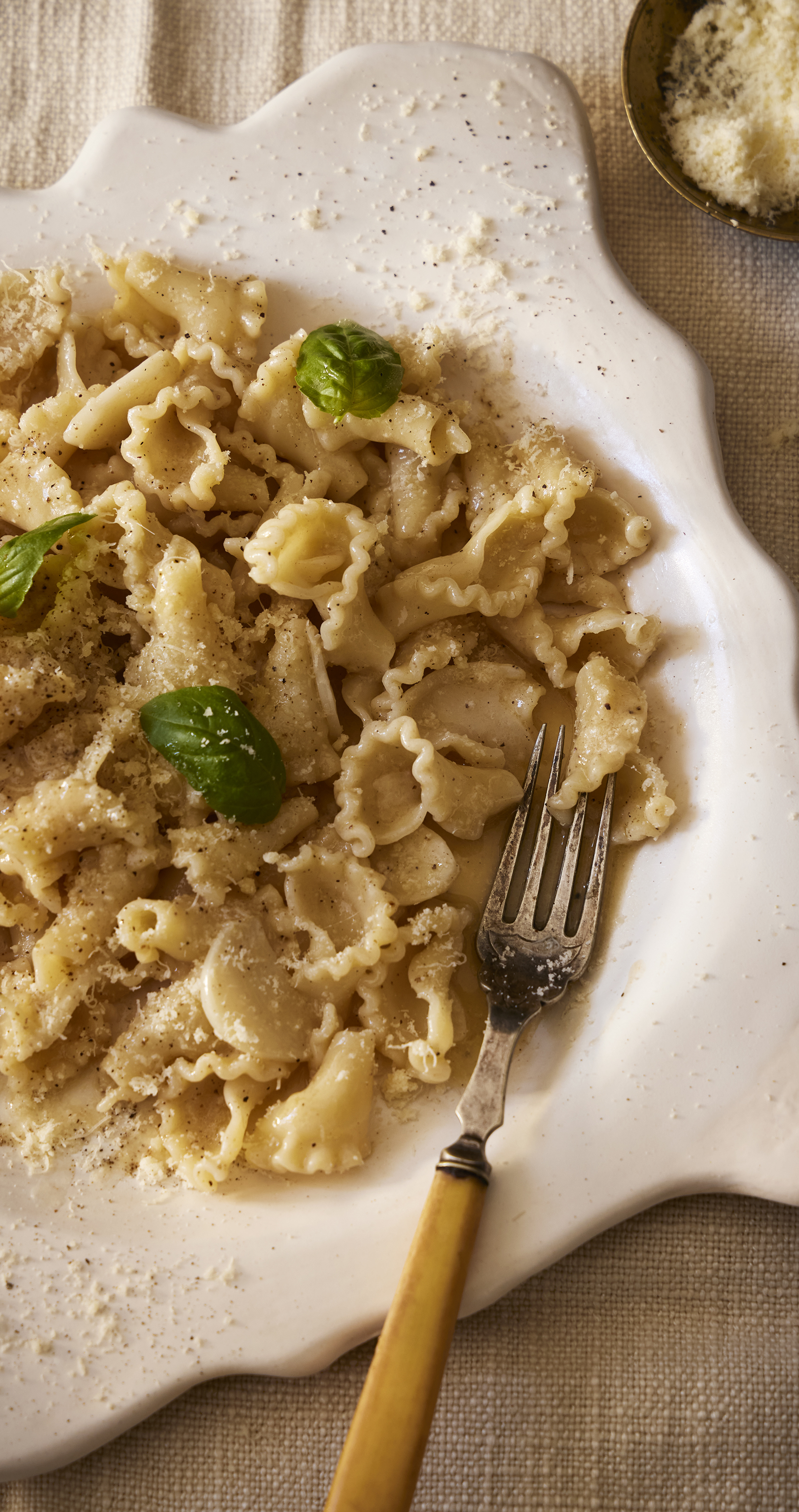 Ruffled pasta with parmesan and fresh basil leaves served on a white scalloped plate with a vintage fork.
