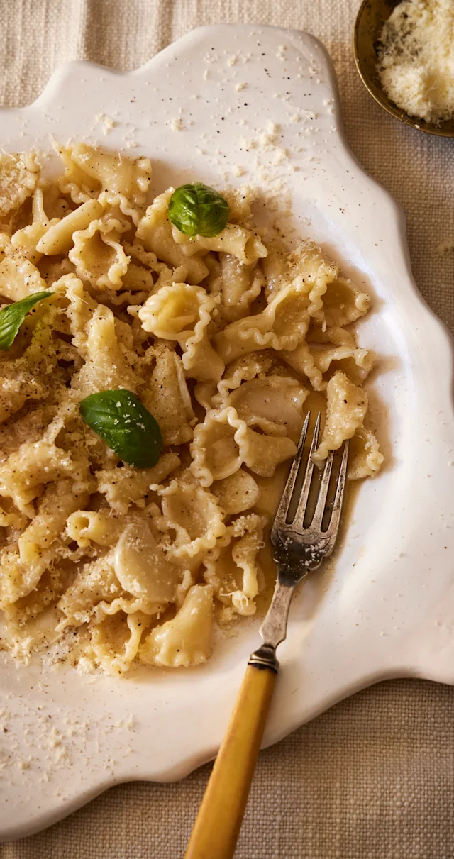 Ruffled pasta with parmesan and fresh basil leaves served on a white scalloped plate with a vintage fork.