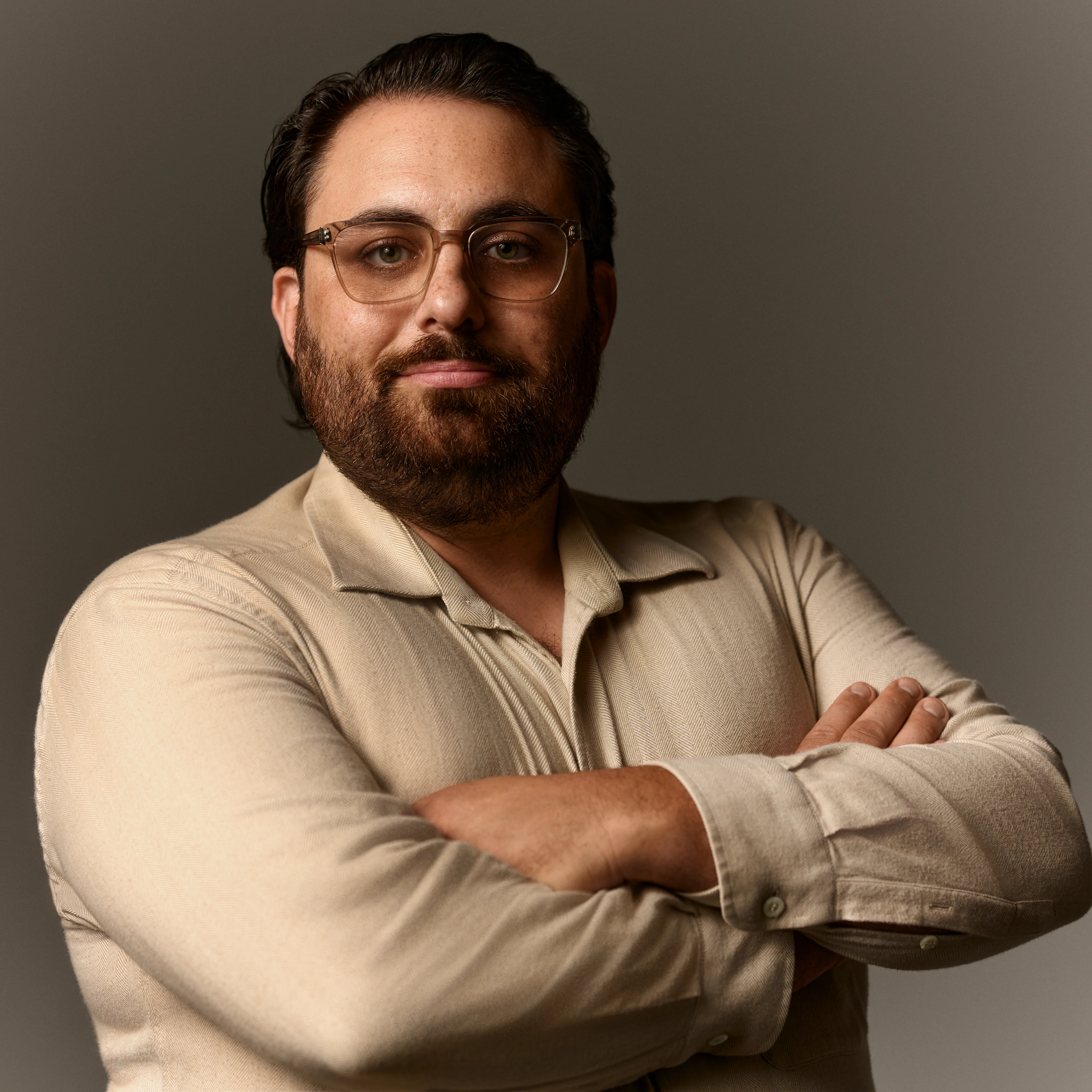Man with brown hair and glasses with his arms crossed