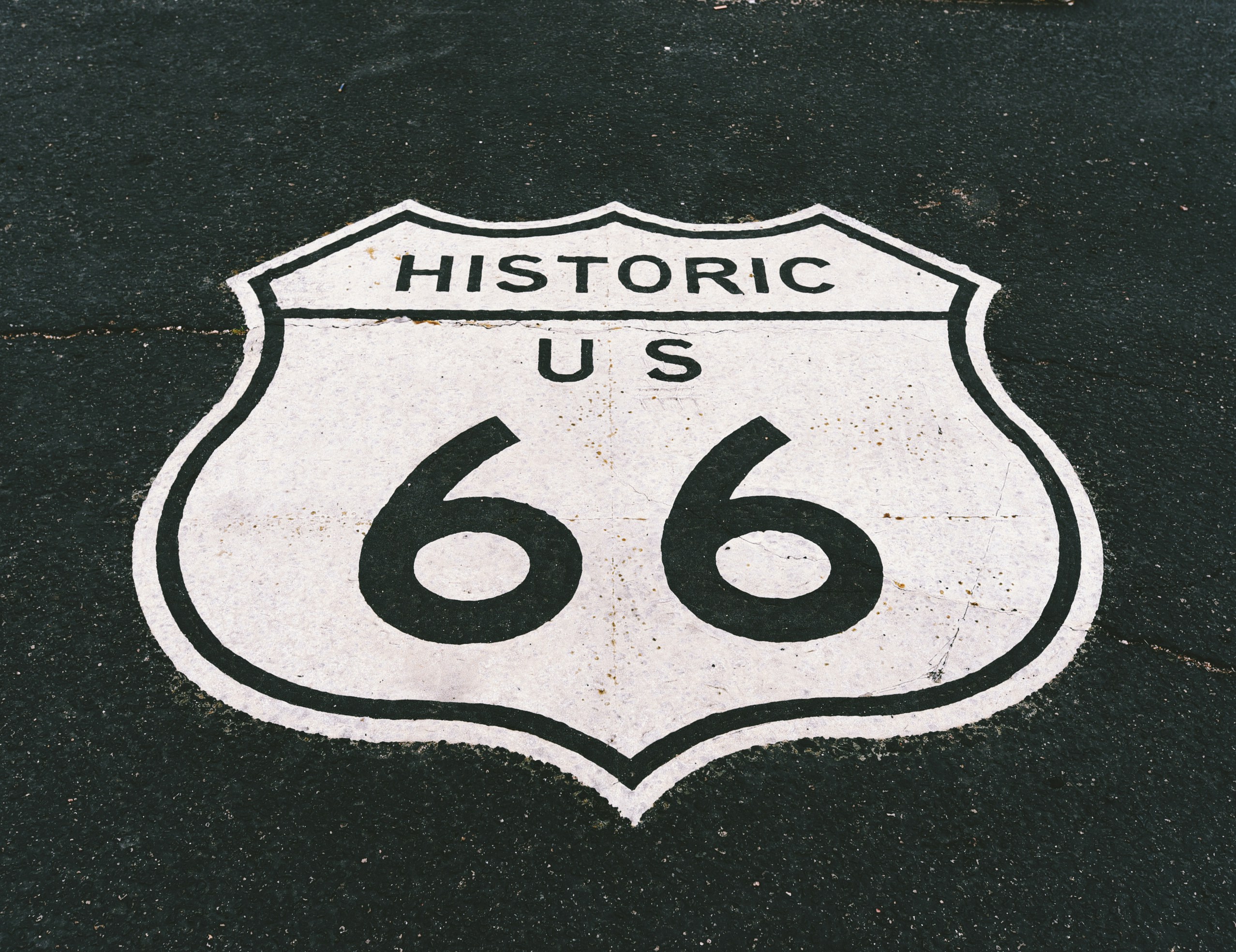 Historic US Route 66 shield logo painted in white on dark asphalt pavement.