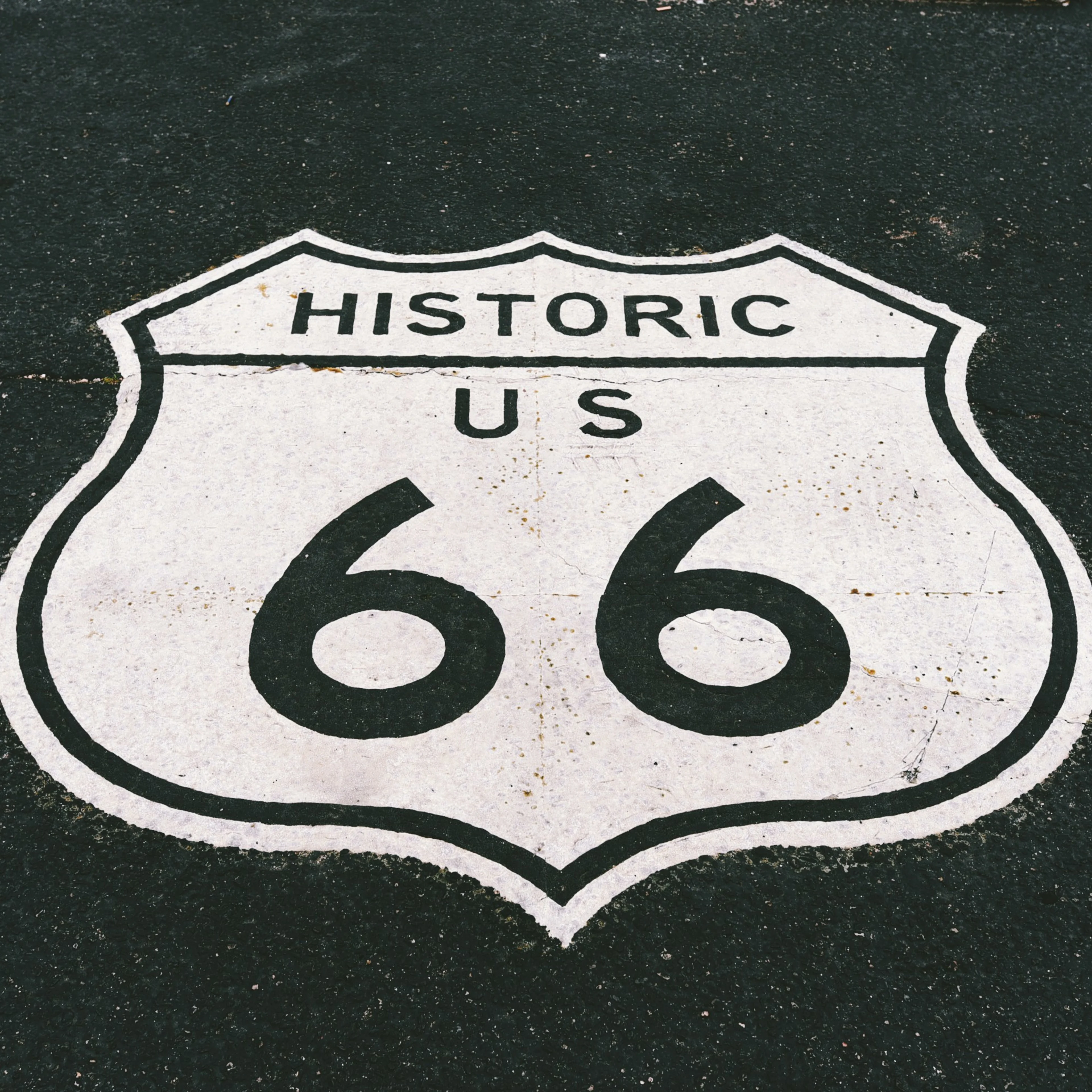 Historic US Route 66 shield logo painted in white on dark asphalt pavement.