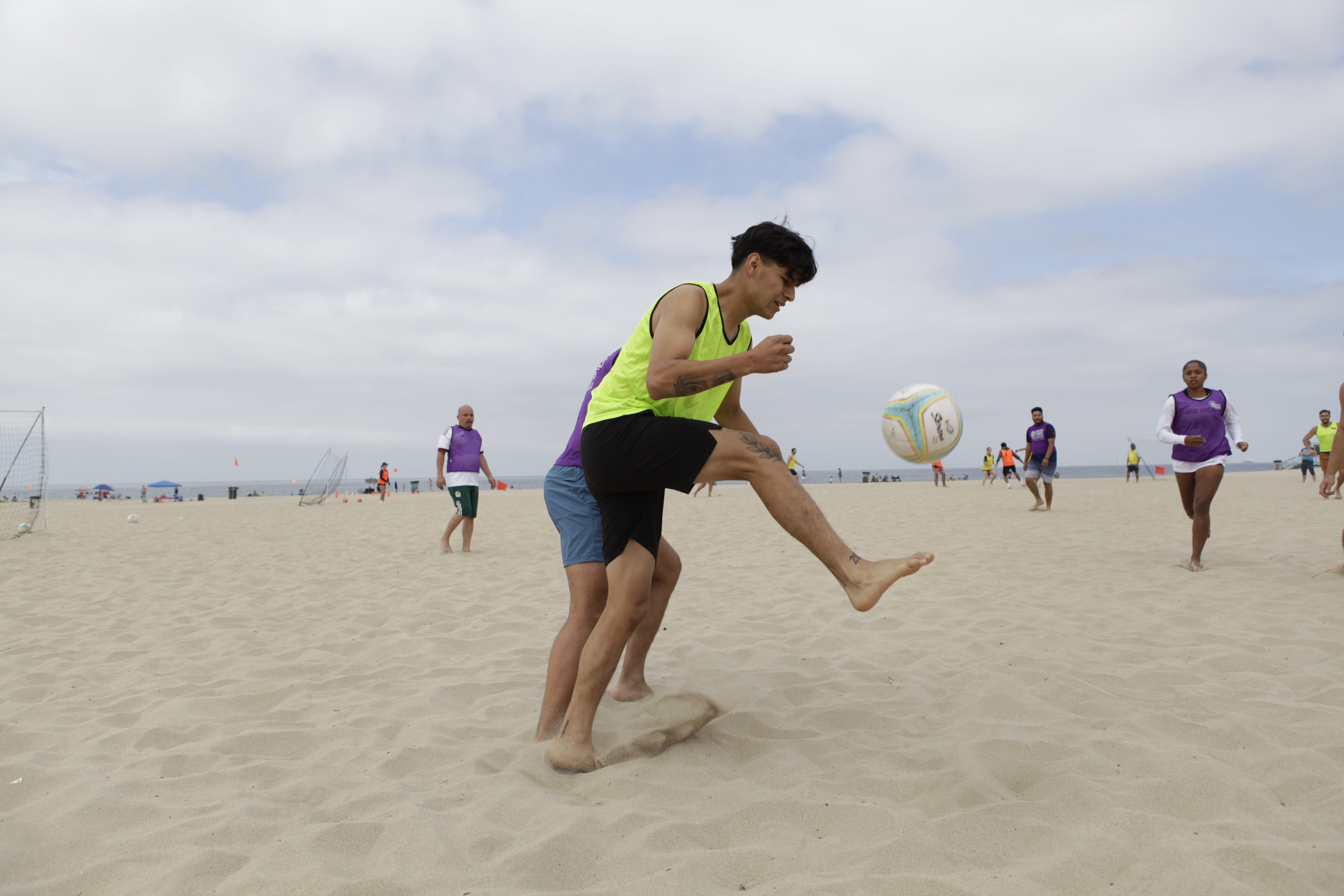 A beach soccer player kicks the ball up off the sand.