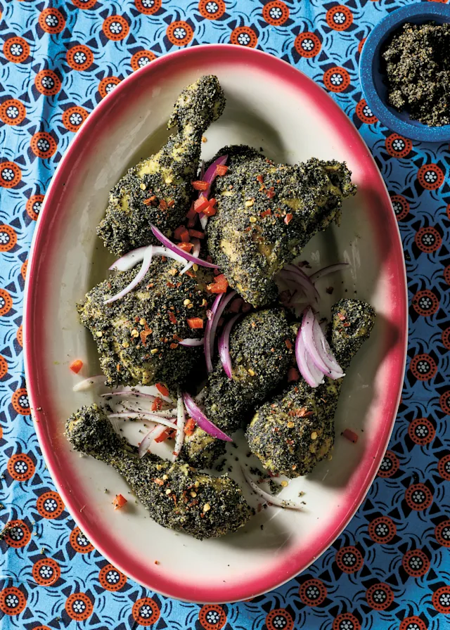 Herb-crusted chicken pieces with red onion slices on a pink-rimmed plate, set on a blue patterned tablecloth.