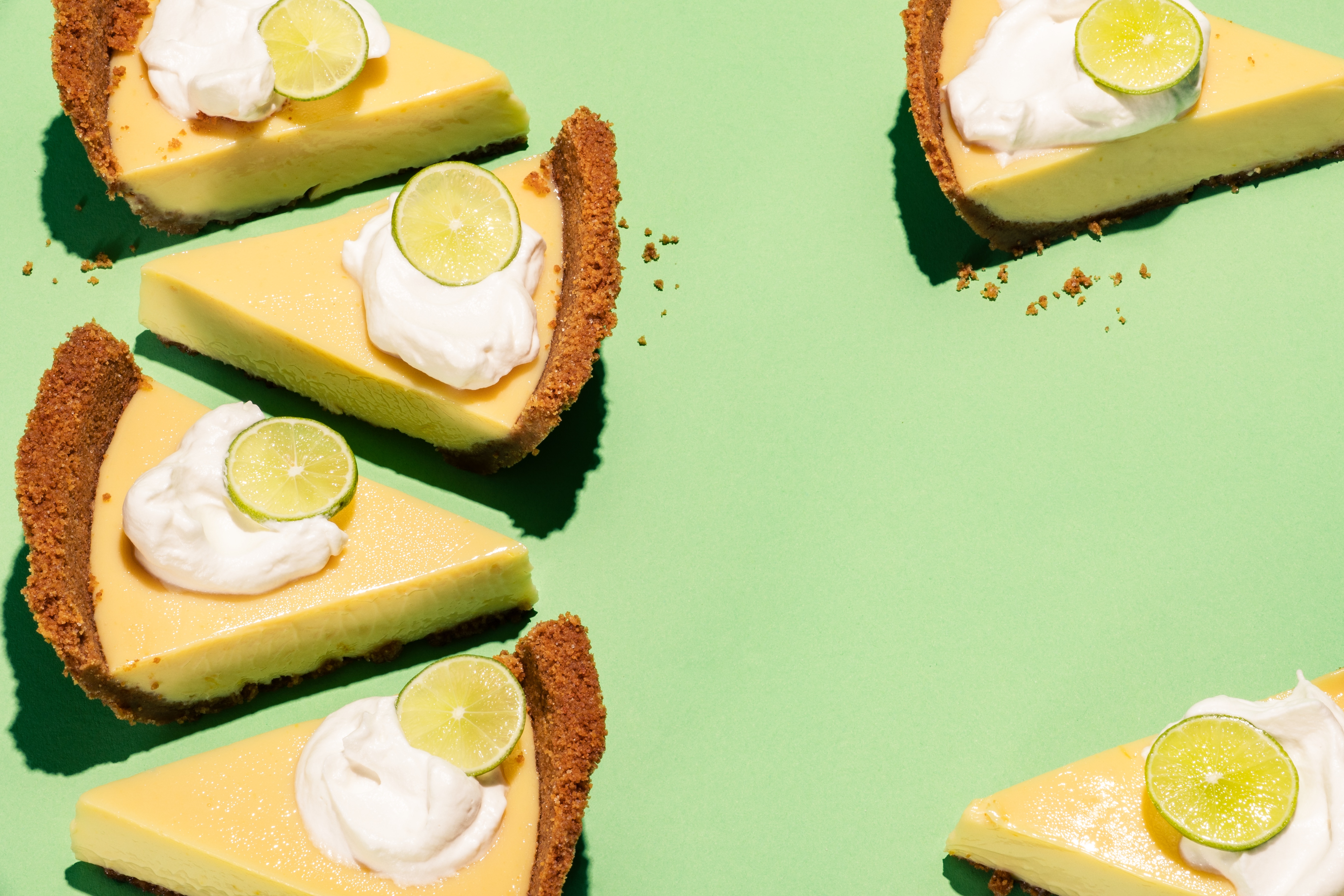 Slices of key lime pie with graham cracker crust and whipped cream topped with lime slices on a green background.