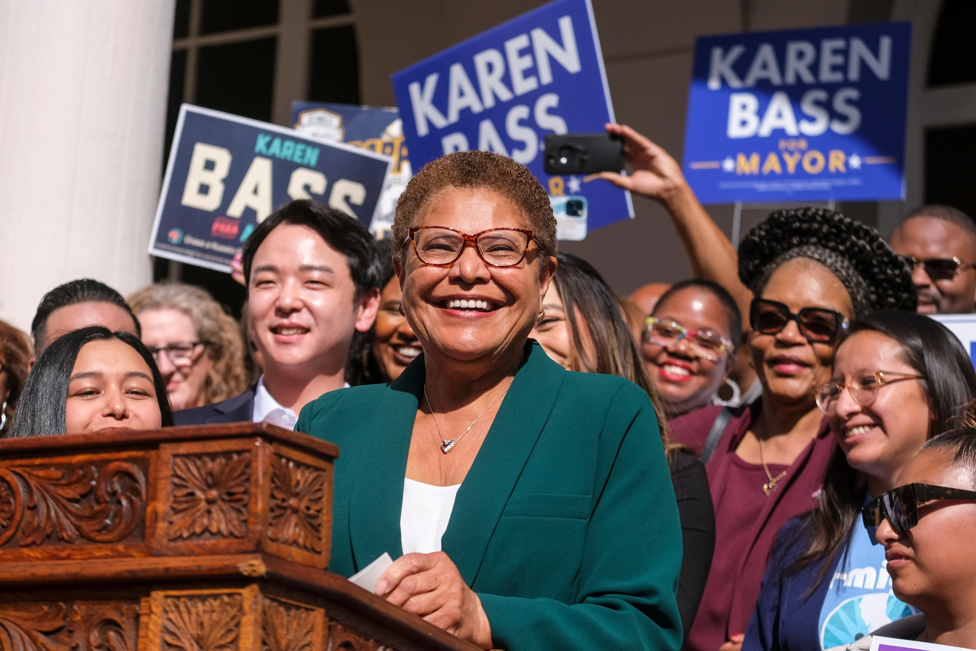 LA Mayor Karen Bass smiling at a podium in a green suit