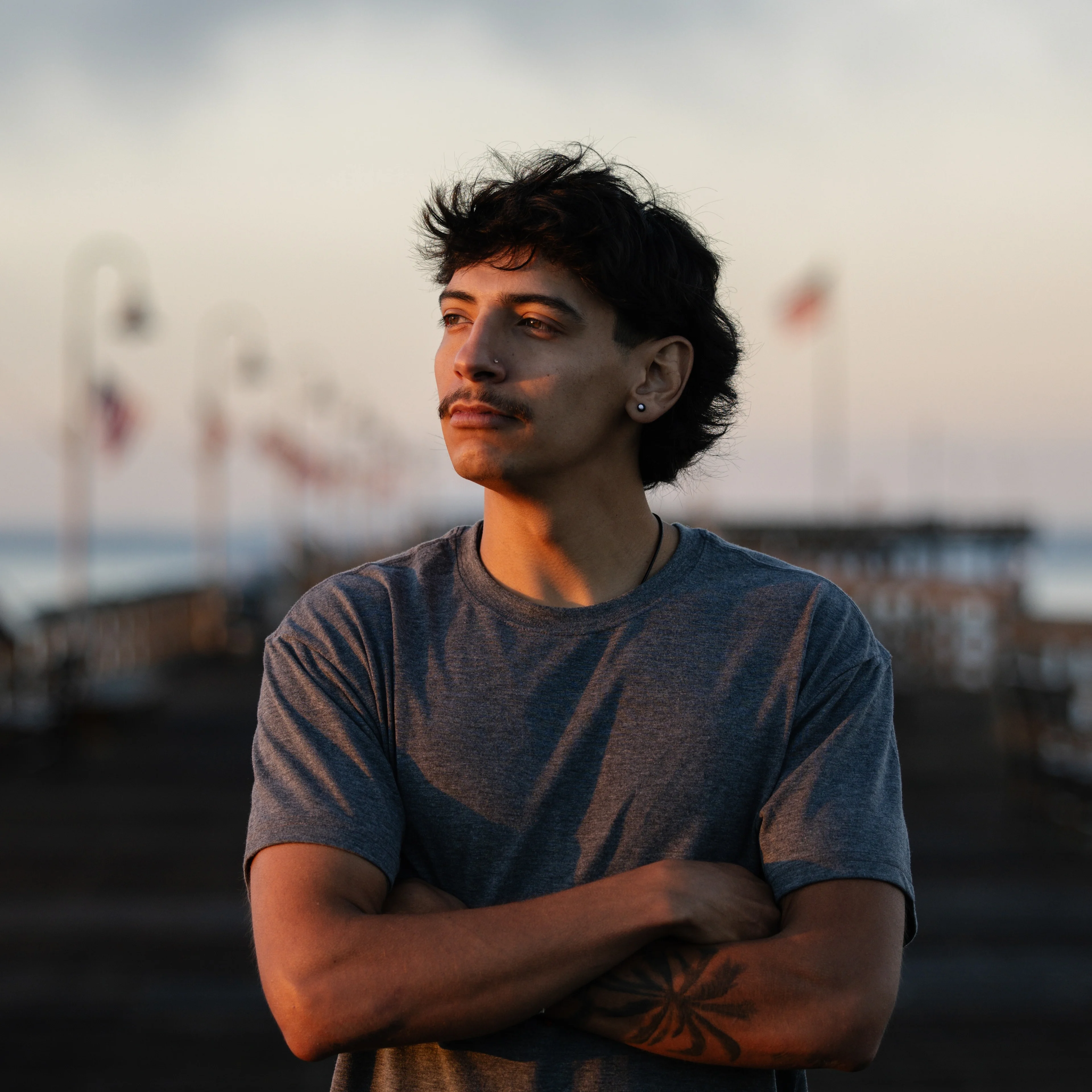 A Latino man with dark, curly hair poses on a wooden boardwalk with American flags in the background.