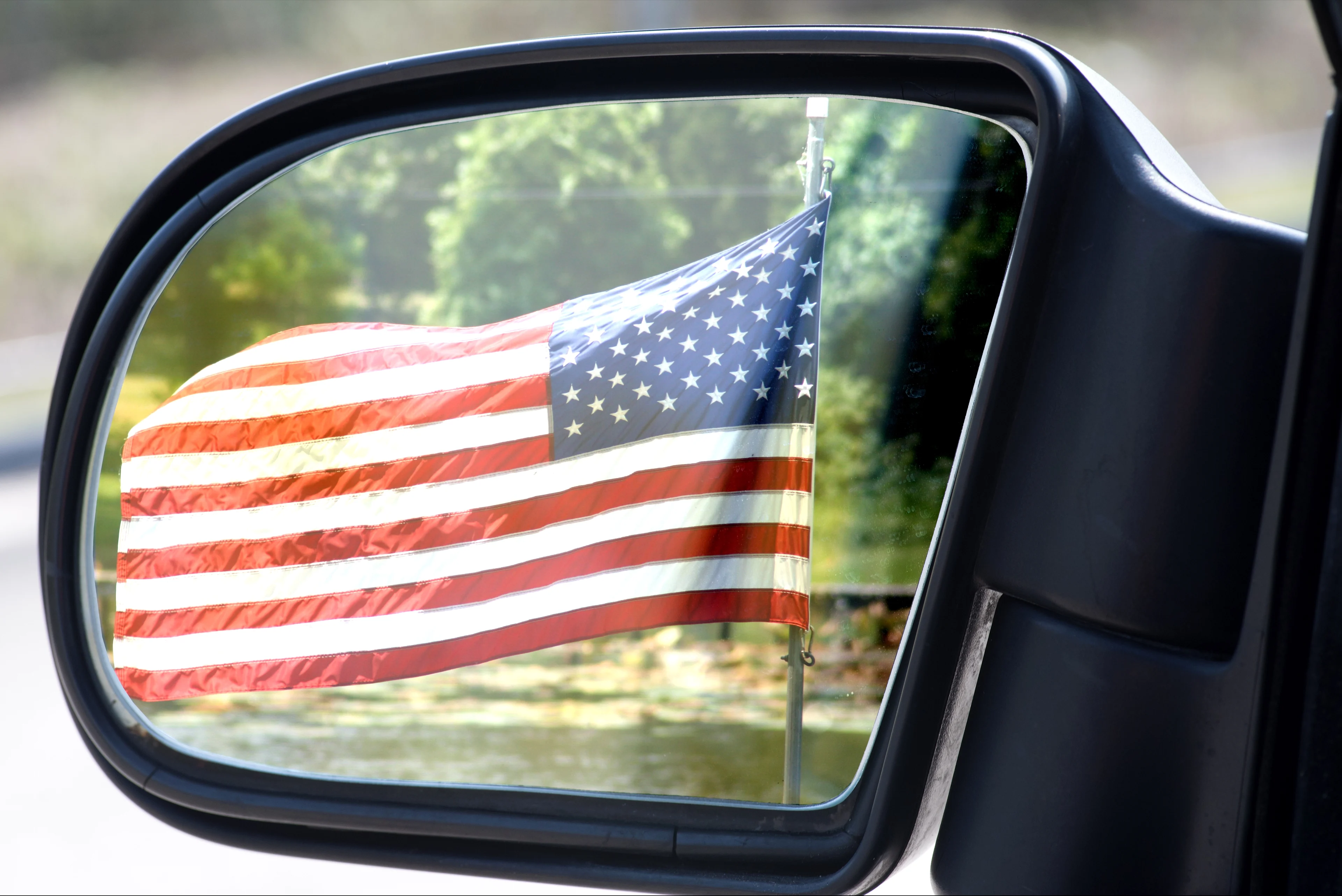 An American flag on display in a car's rearview mirror.