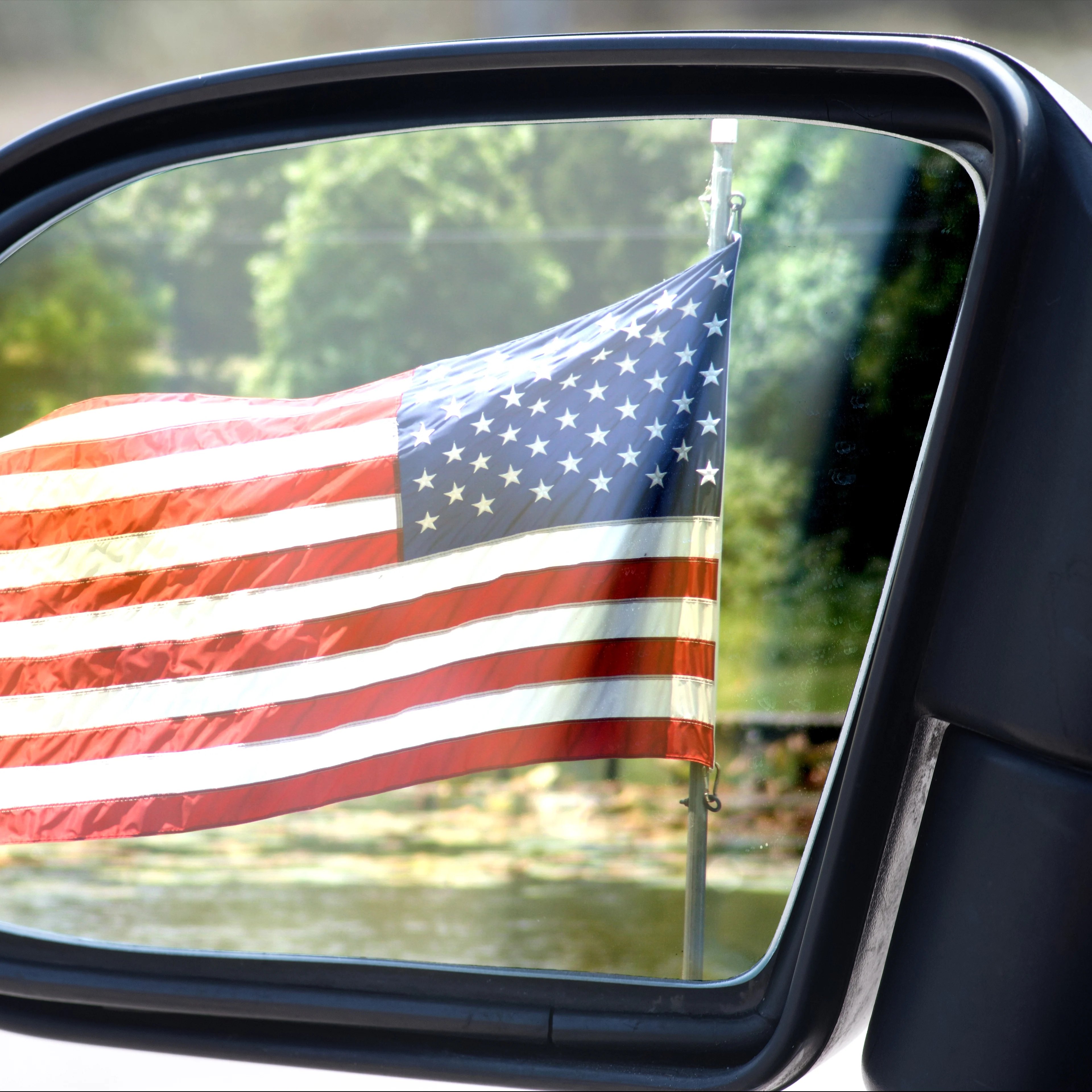An American flag on display in a car's rearview mirror.