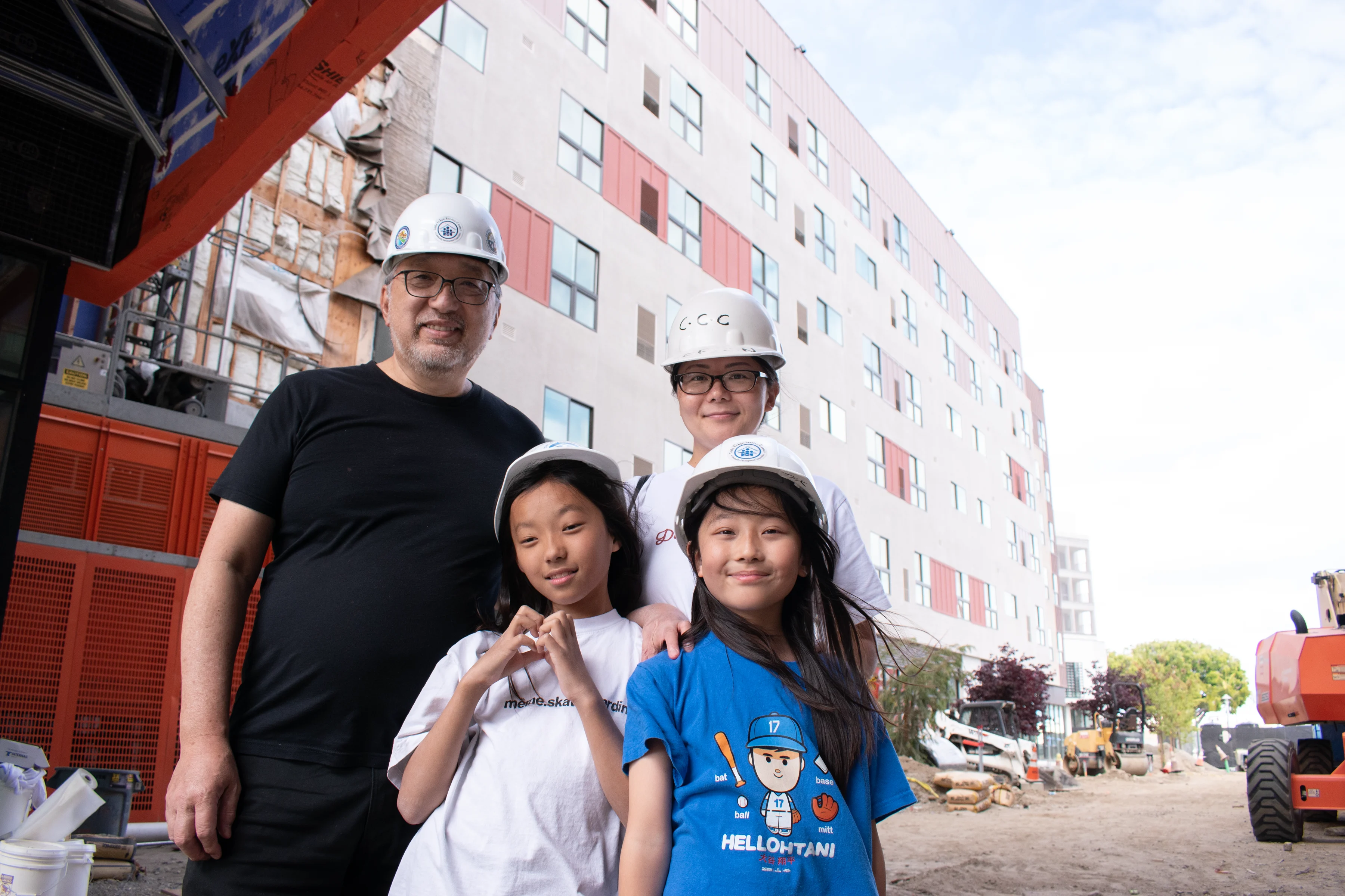 A man, woman, and two children stand together wearing hard hats at a construction site