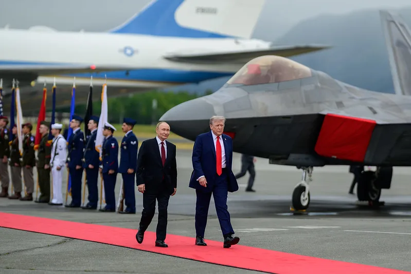 Two men in dark suits walk down a red carpet.