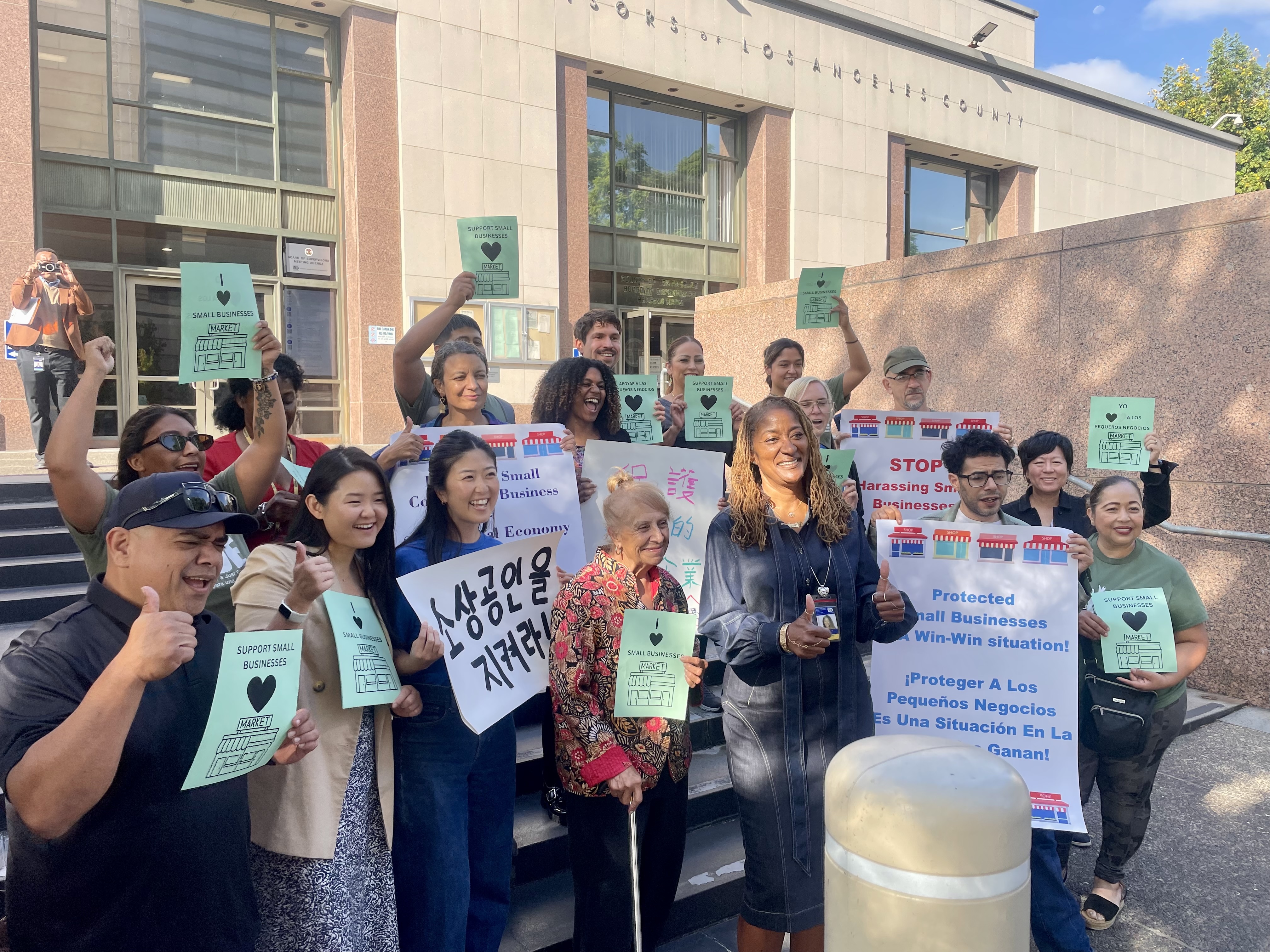 A group of adults hold signs and pose with LA County Board of Supervisor Holly Mitchell in front of the Board of Supervisors hearing room