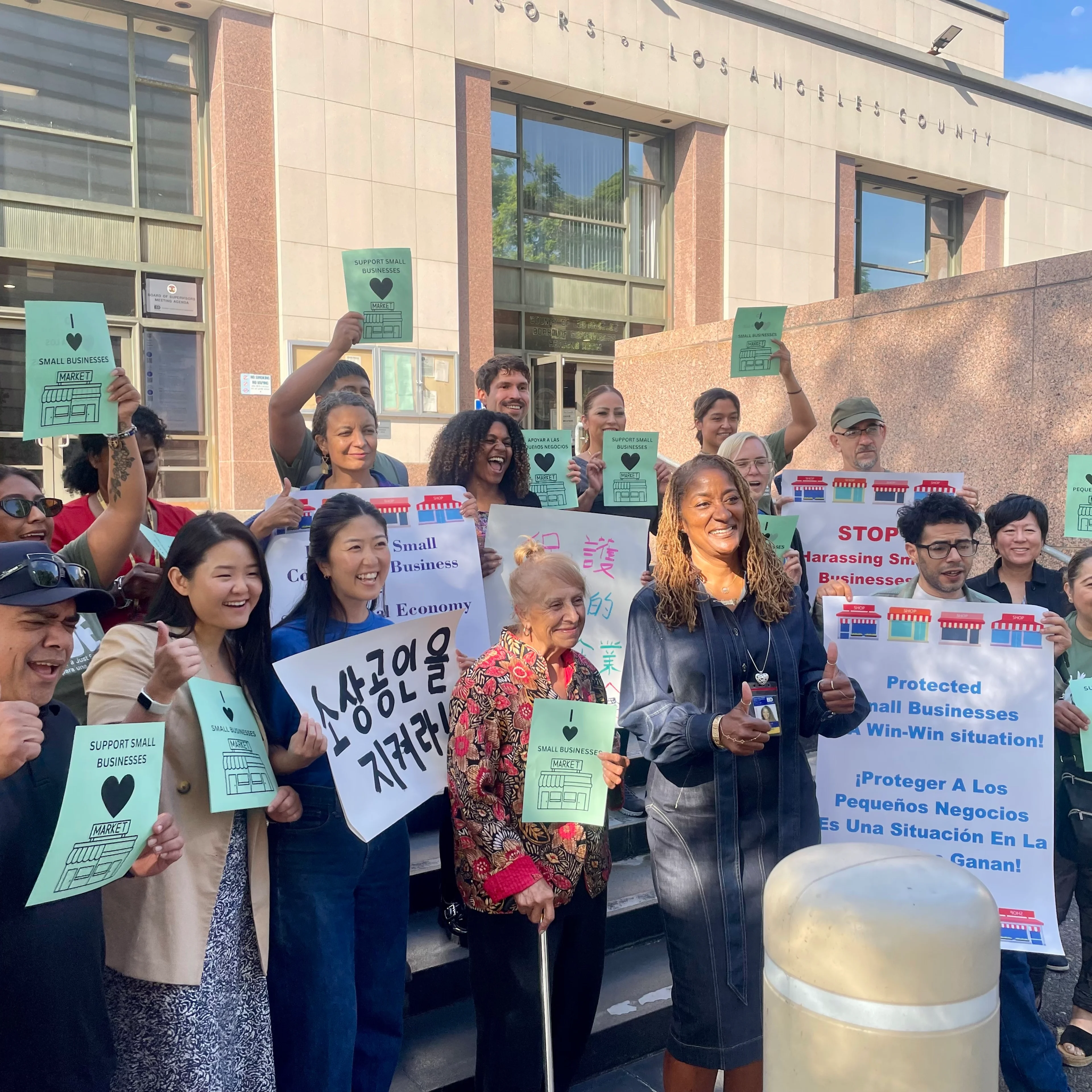 A group of adults hold signs and pose with LA County Board of Supervisor Holly Mitchell in front of the Board of Supervisors hearing room