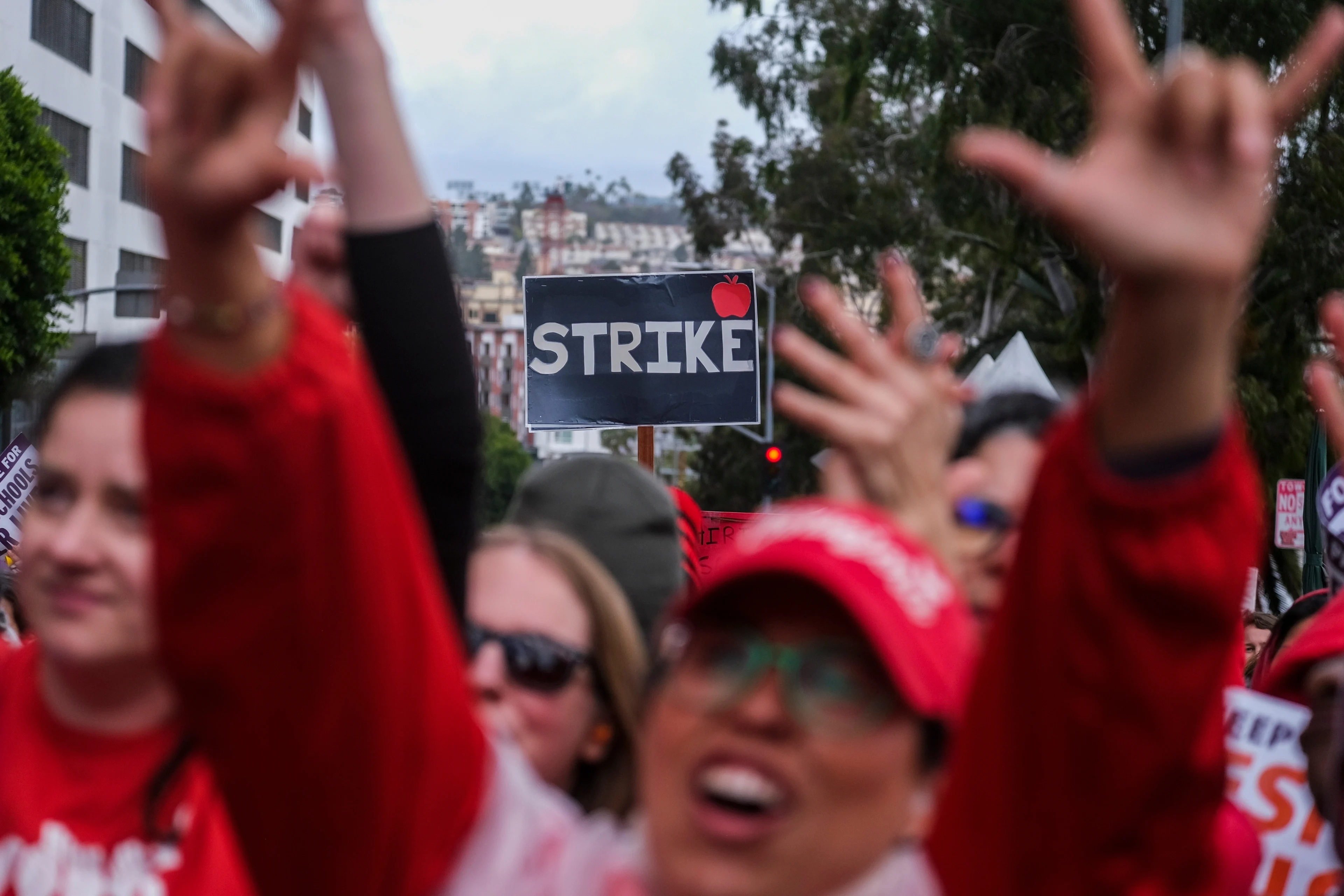 A crowd of teachers walks outside in downtown LA. The picture focuses on a sign that reads 'STRIKE.;