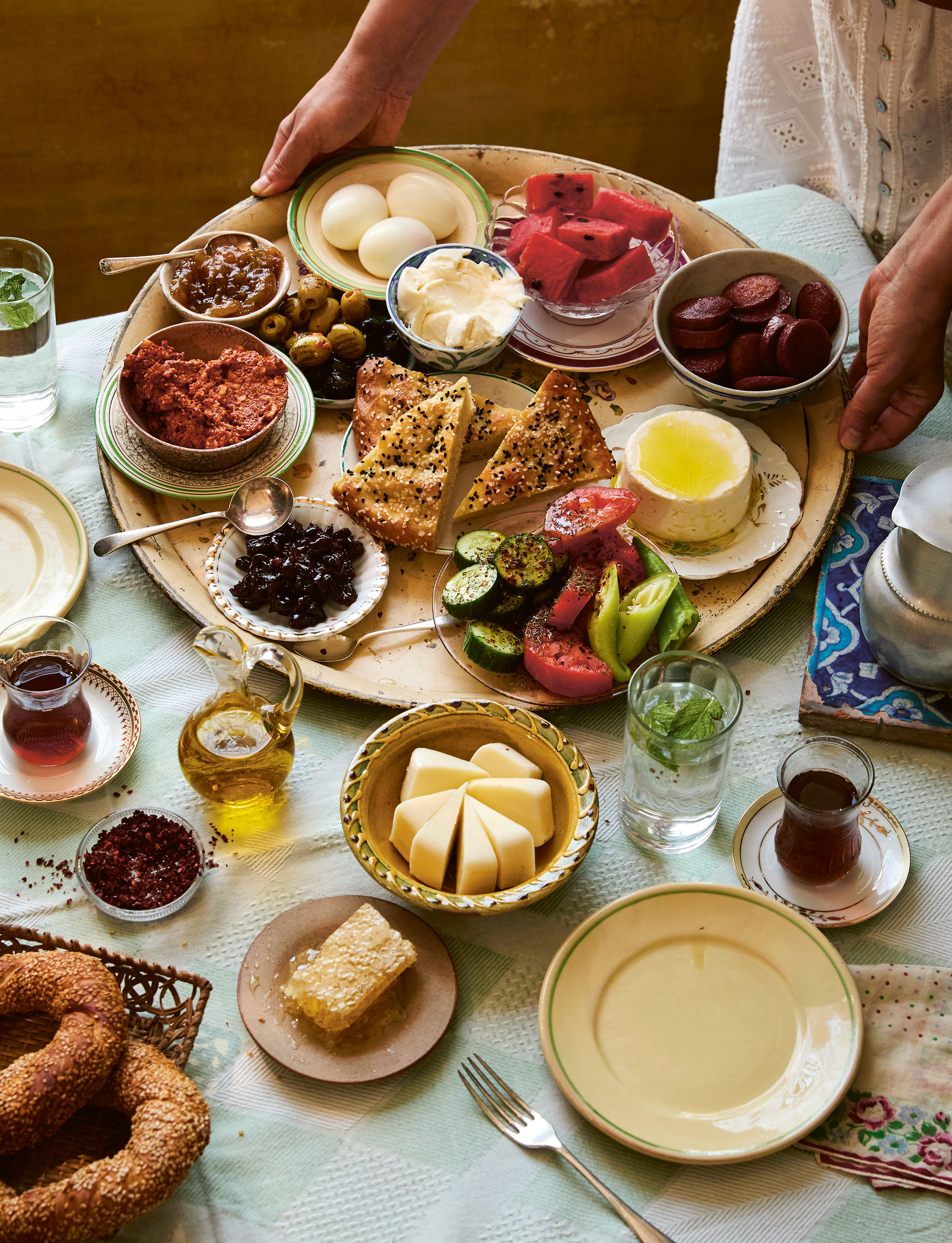 A spread of Turkish breakfast foods on a table, including cheeses, olives, eggs, vegetables, pastries, jams, and tea.