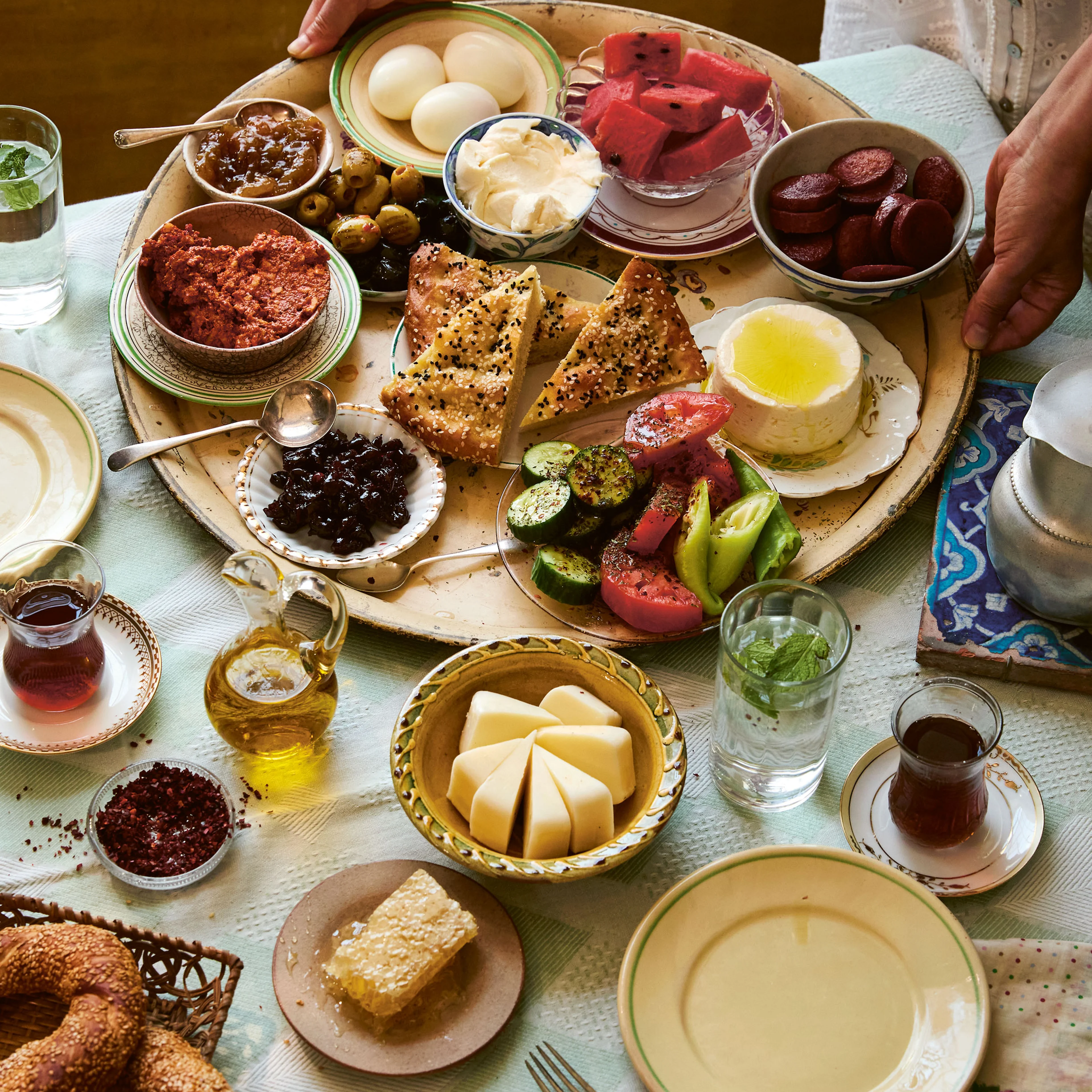 A spread of Turkish breakfast foods on a table, including cheeses, olives, eggs, vegetables, pastries, jams, and tea.