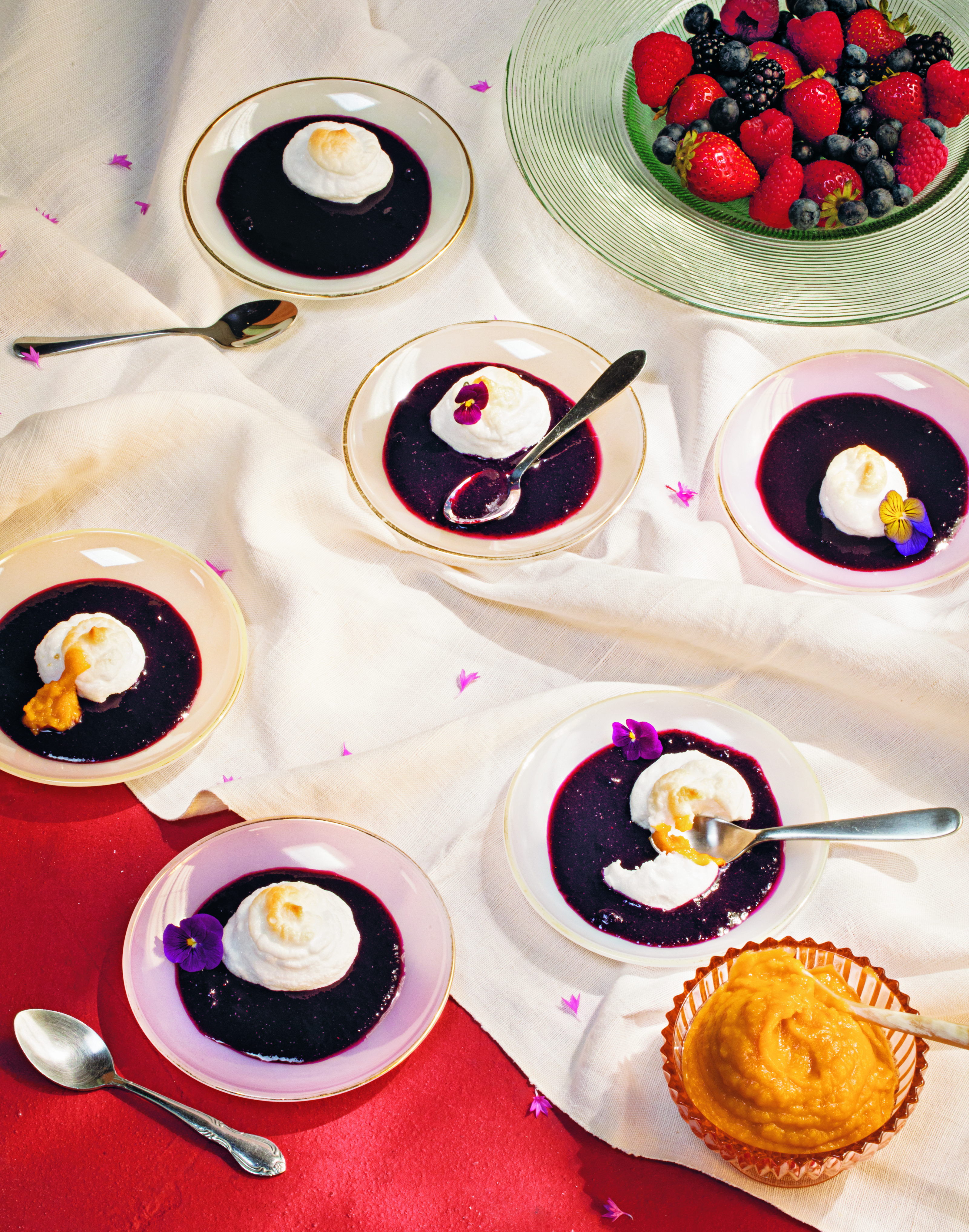 Berry desserts with whipped cream in small dishes, alongside fresh berries in a glass bowl and a small tart.