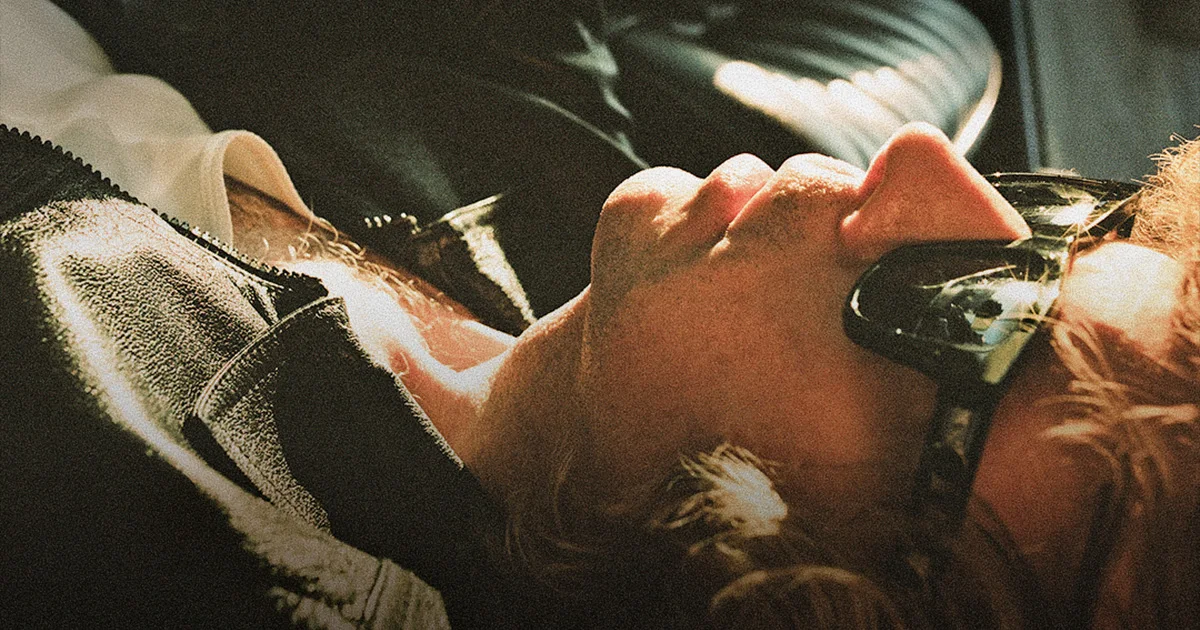 Beck lying back, wearing dark sunglasses, bathed in warm golden light with a moody, cinematic tone.