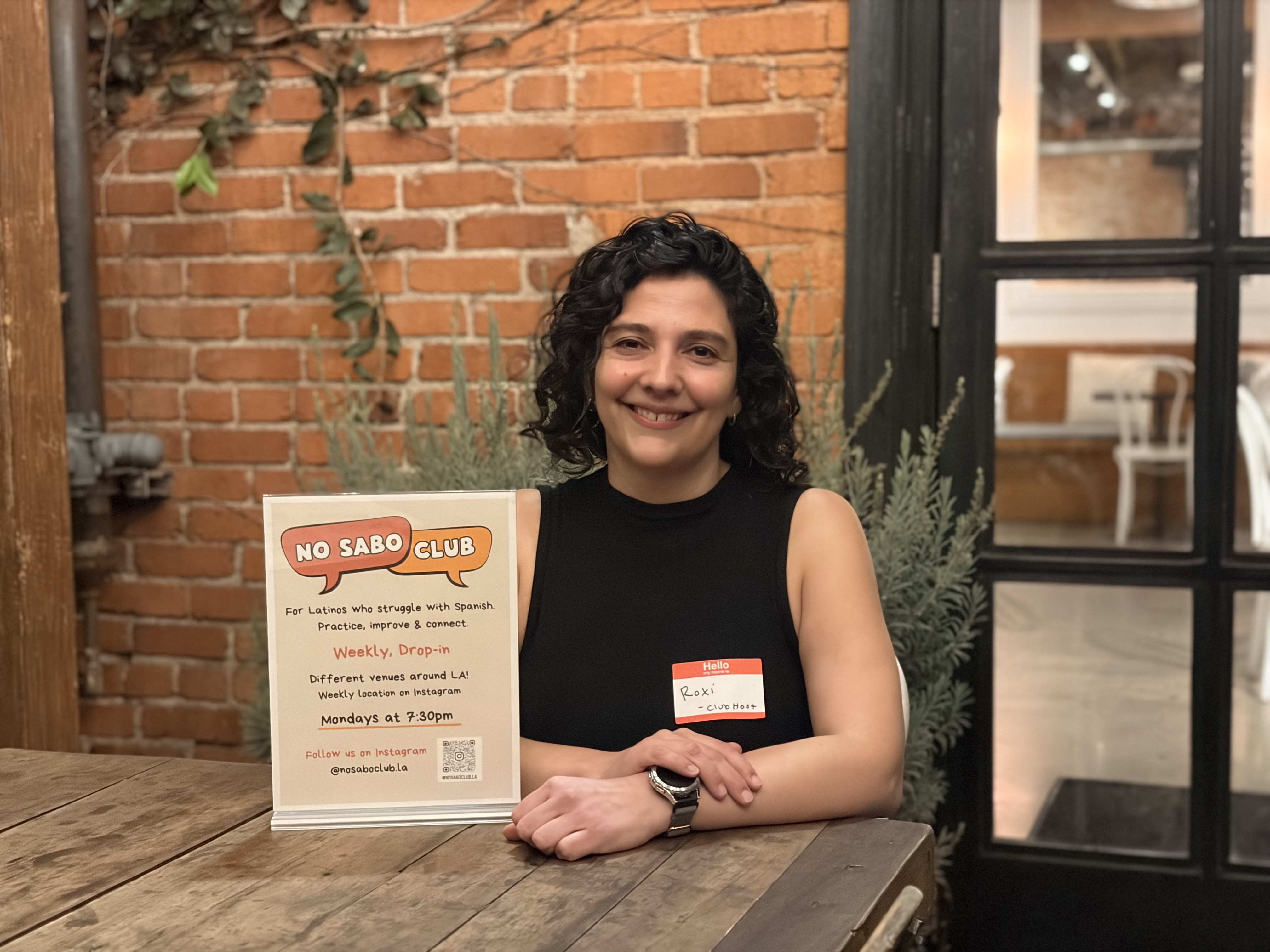Photo of a woman sitting at a table with her arms crossed in front of her and smiling. 