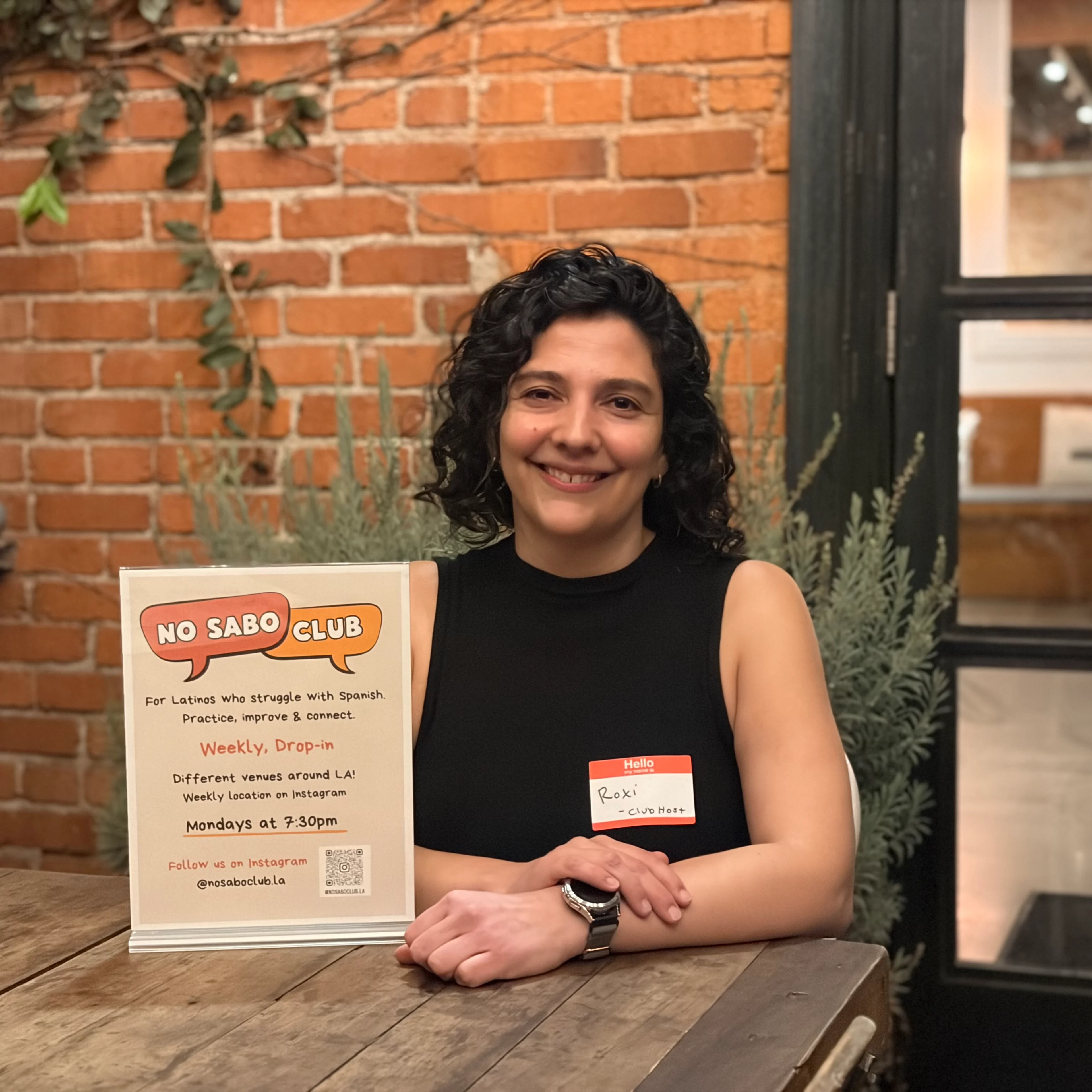 Photo of a woman sitting at a table with her arms crossed in front of her and smiling.