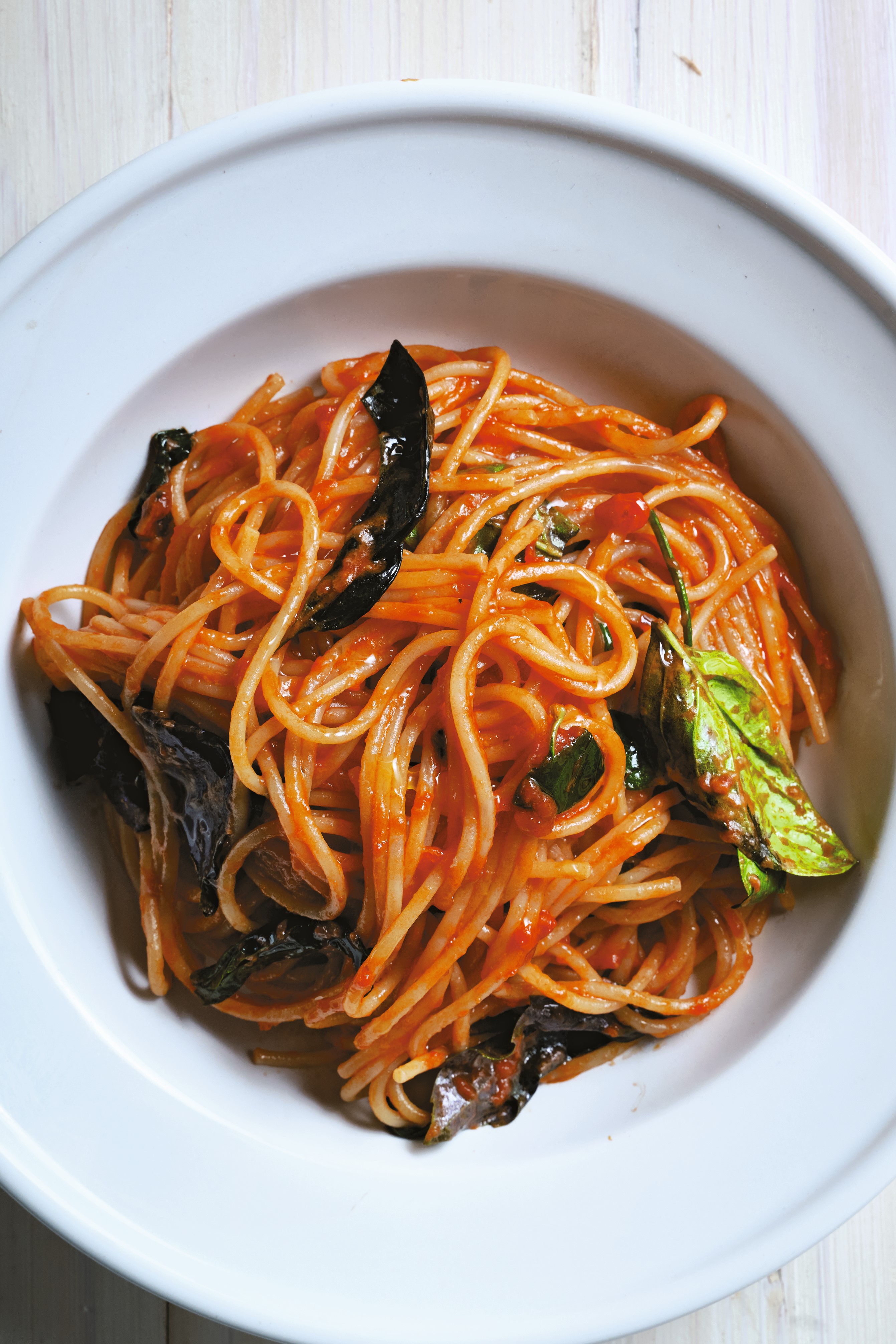 Spaghetti in tomato sauce with fresh basil leaves served in a white bowl on a wooden surface.
