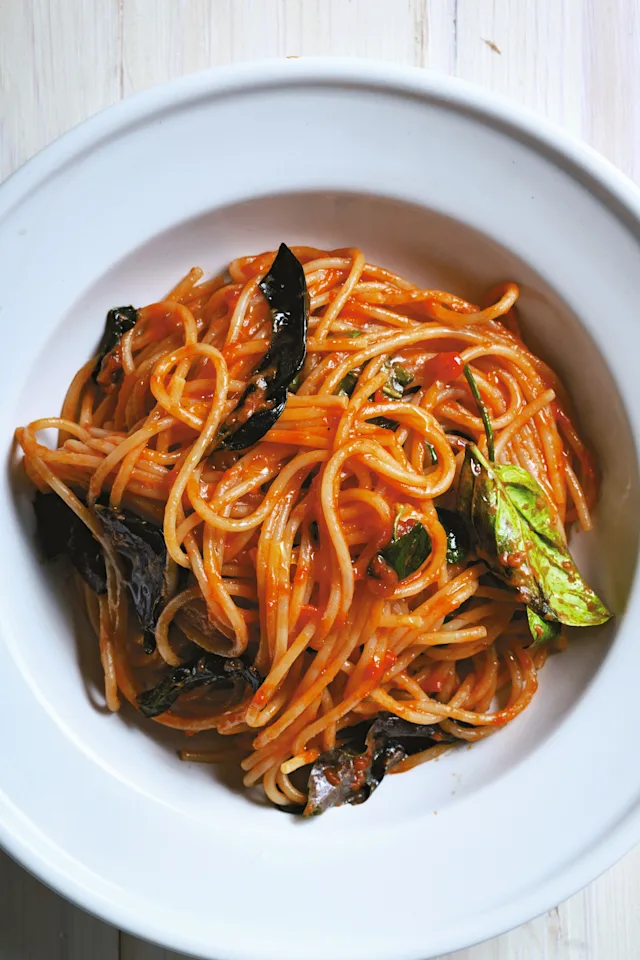 Spaghetti in tomato sauce with fresh basil leaves served in a white bowl on a wooden surface.