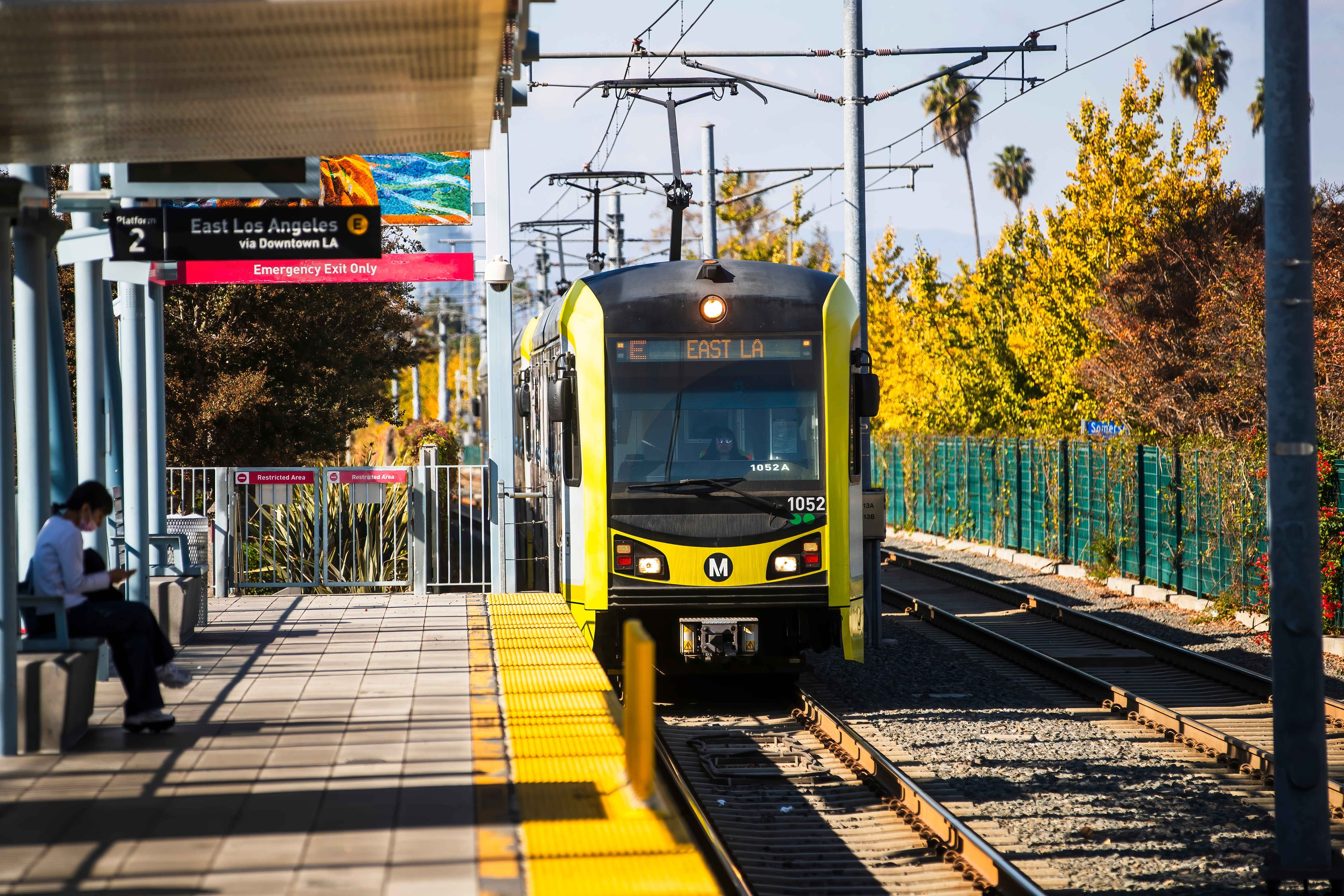 An LA Metro train pulls up to a station while a customer waits.